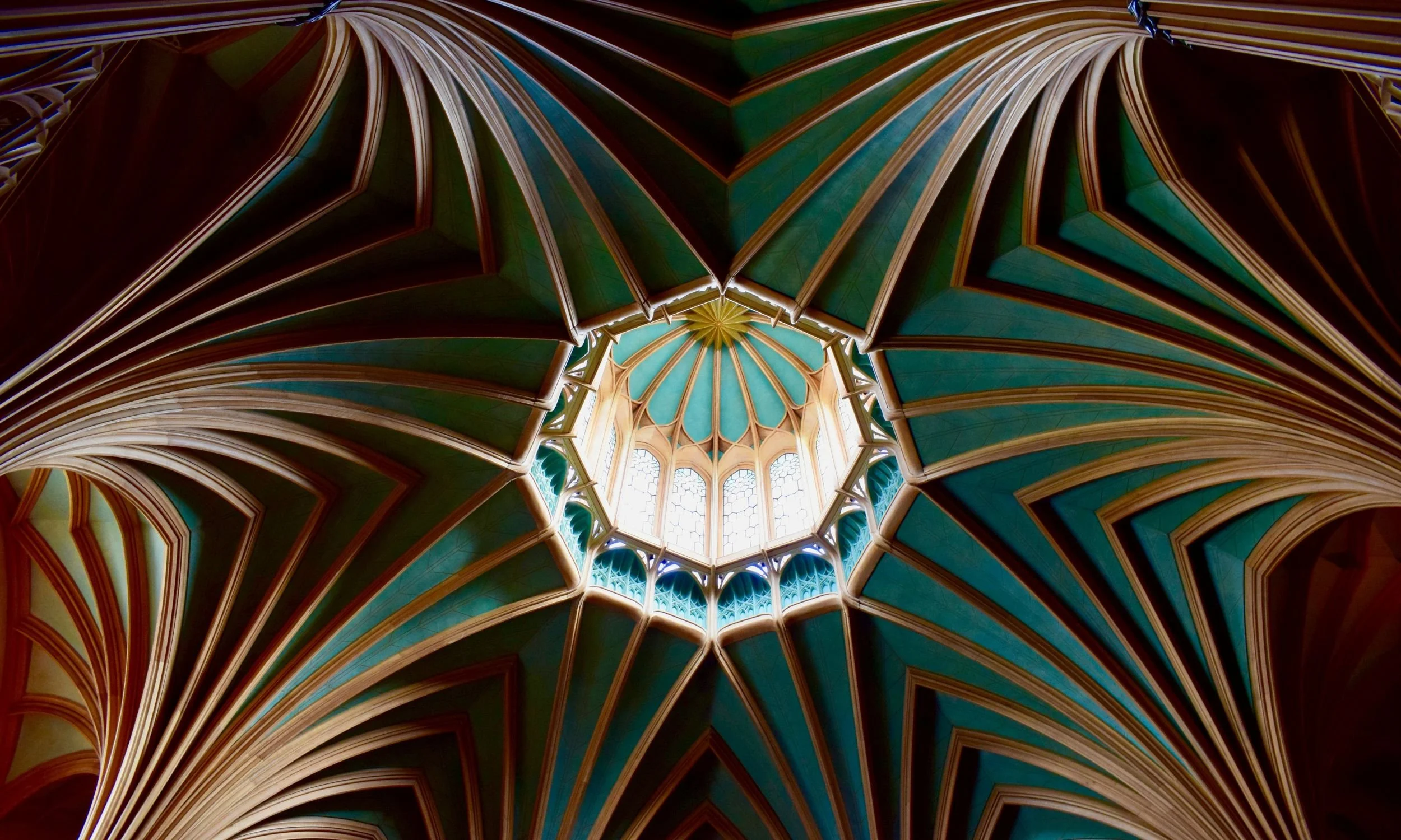 View of an ornate, colorful architectural ceiling with a large, circular stained-glass window at the top center.