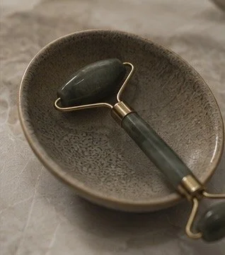 A jade facial roller resting inside a ceramic bowl.