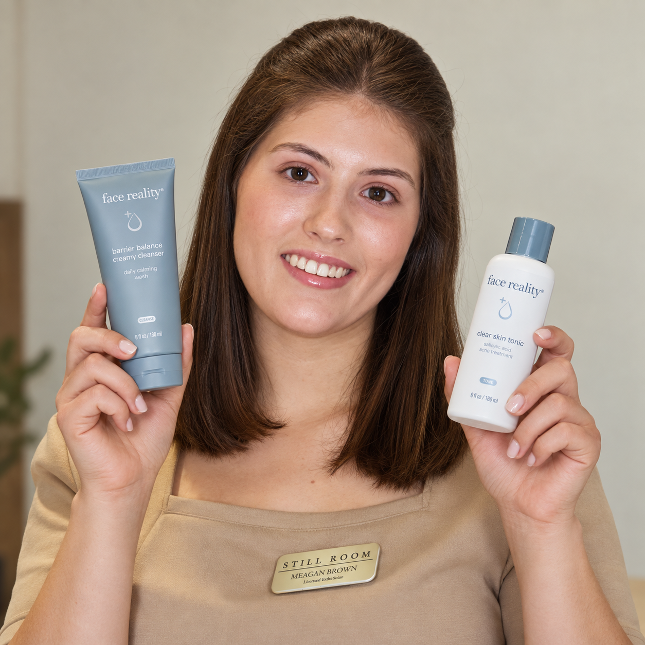 A woman with brown hair holding skincare products in each hand, smiling at the camera, wearing a beige shirt and a name tag that reads "STILL ROOM MEAGAN BROWN."