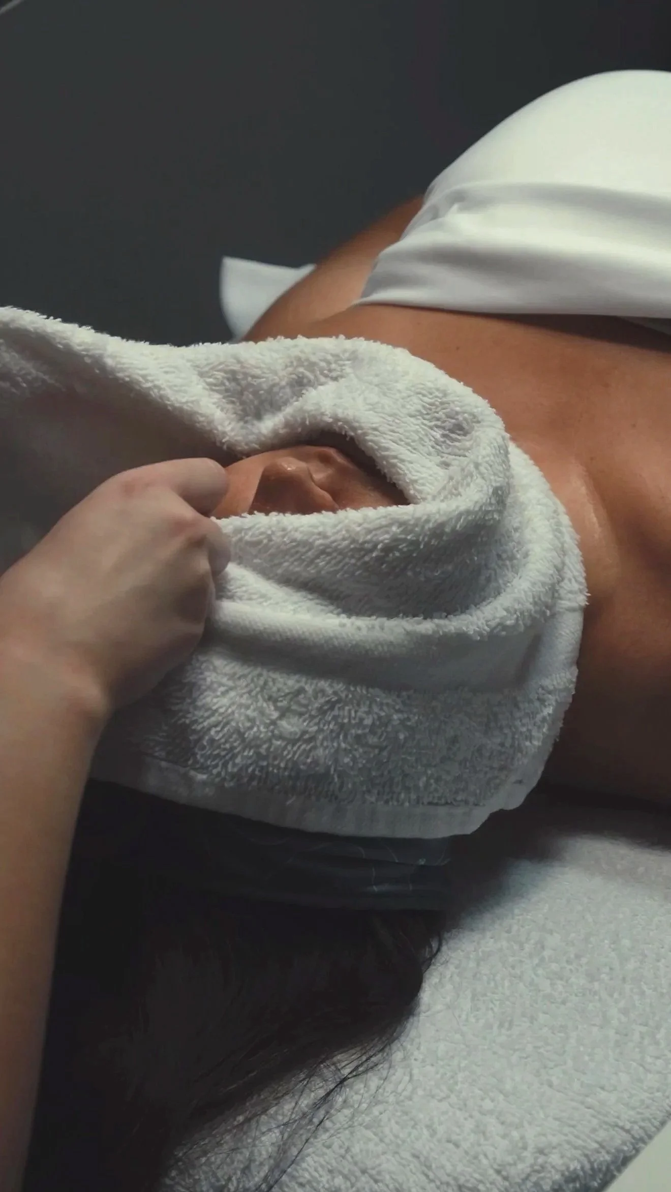A person lying face down on a massage table, covered with a white towel, receiving a massage.