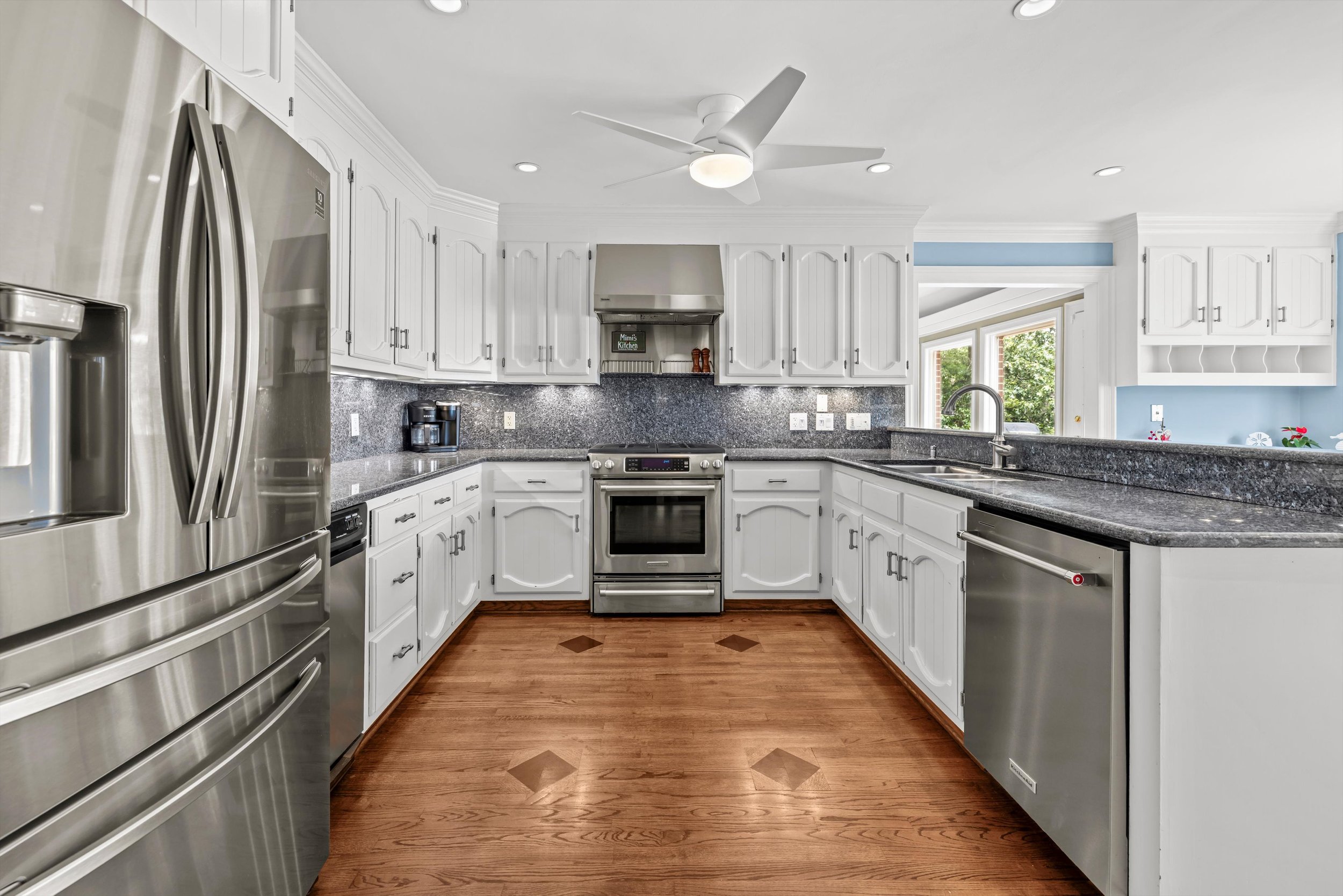 Kitchen with white cabinets, stainless steel appliances, granite countertops, hardwood floor, and a ceiling fan.