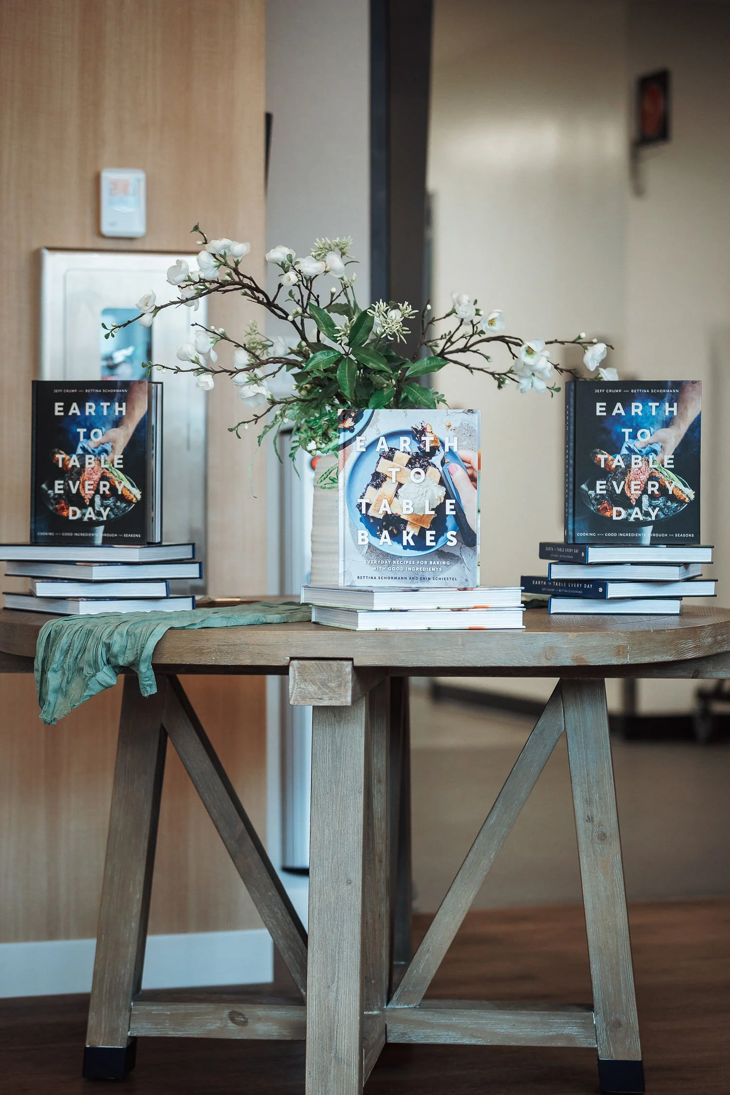 Table with a vase of white flowers and three stacks of books titled 'Earth to Table Bakes' on each side.