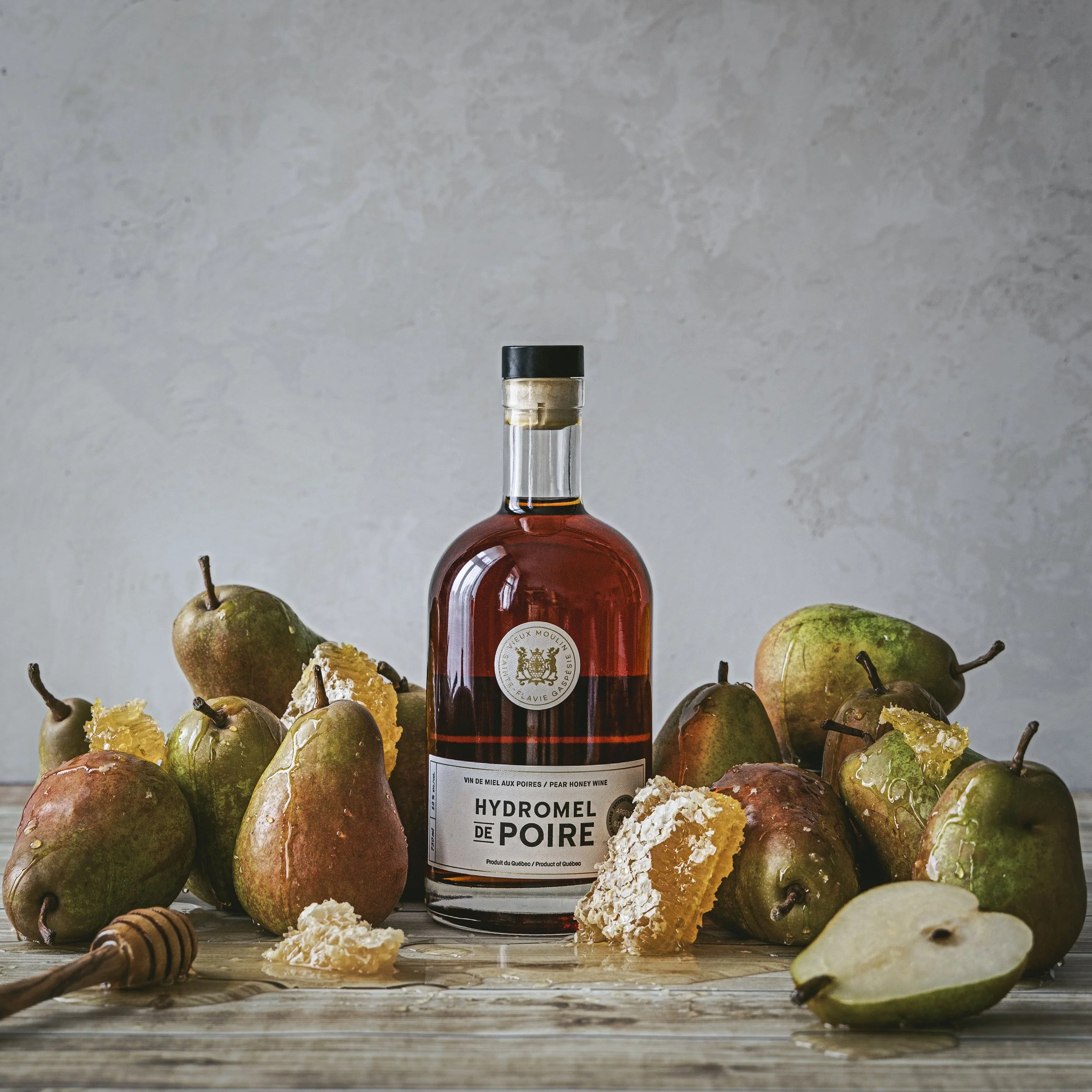 A bottle of pear honey wine surrounded by pears and pear crumbs on a wooden surface.