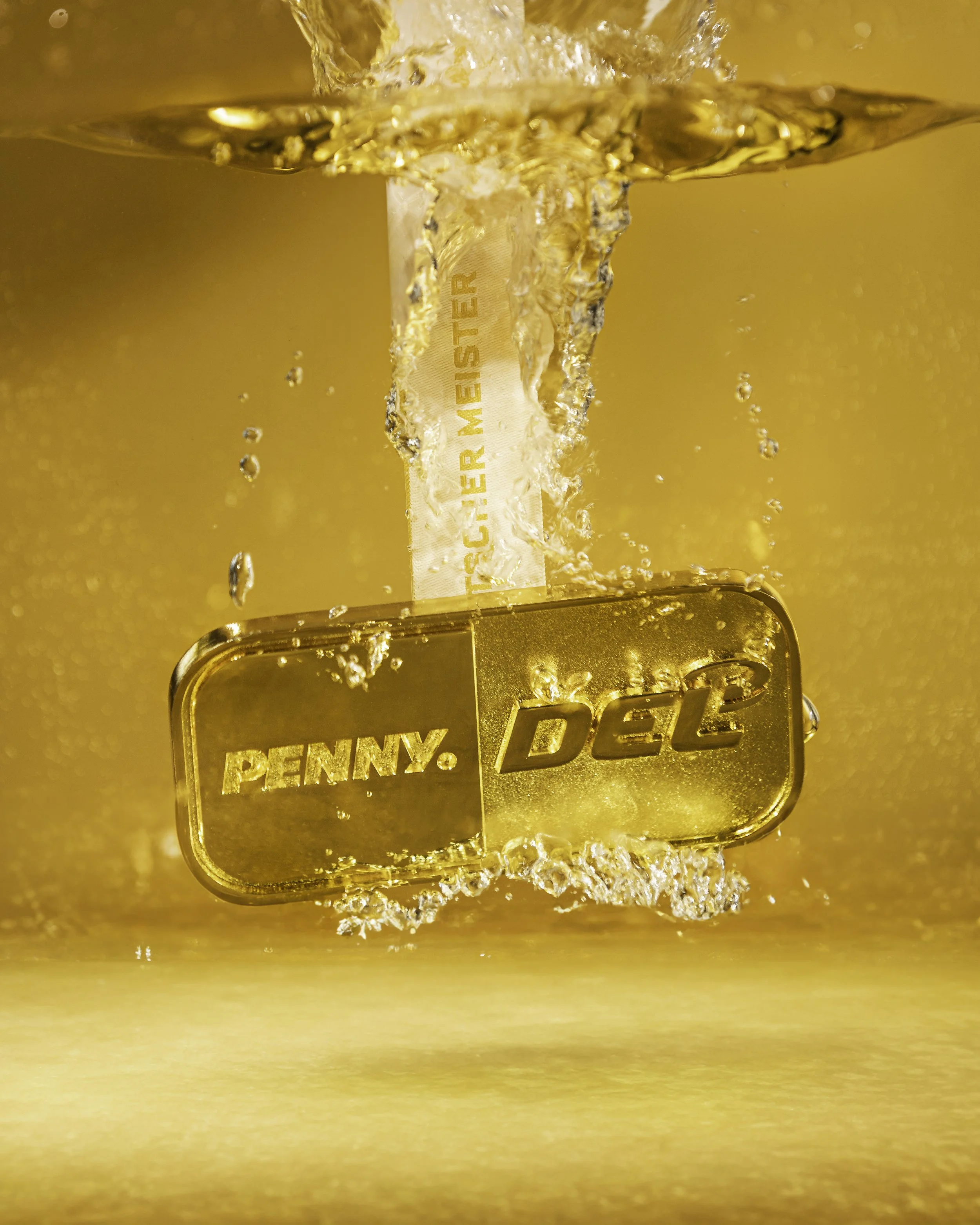 Golden Penny Del sign appears underwater in a splash of water with gold background.