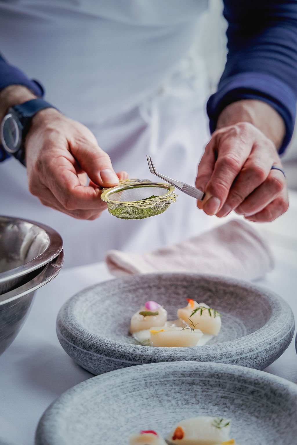 Chef's hands garnishing small, fancy dishes with herbs and sauce in a professional kitchen.