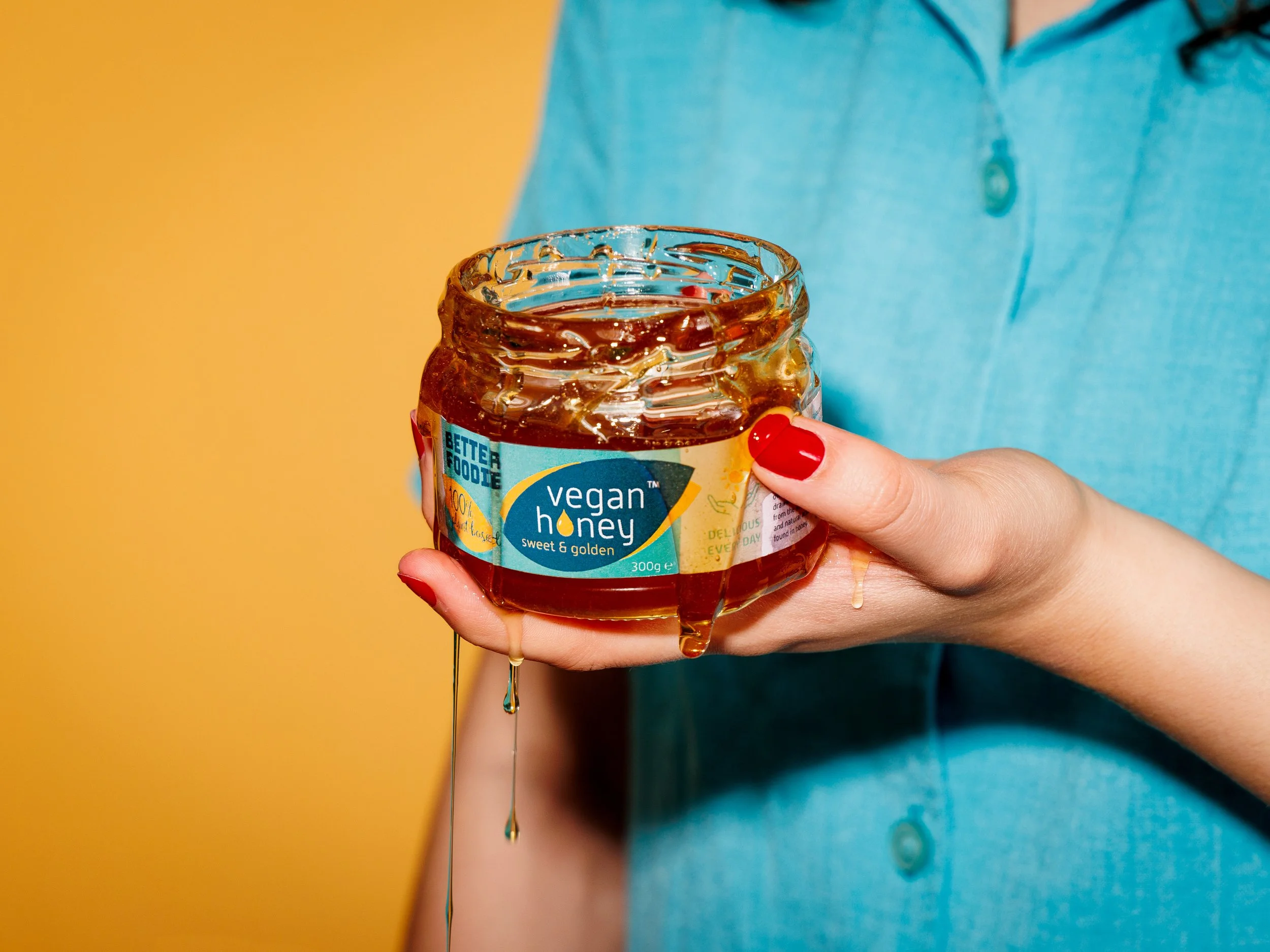 A person in a blue shirt holding an open jar of honey with honey dripping from the jar.