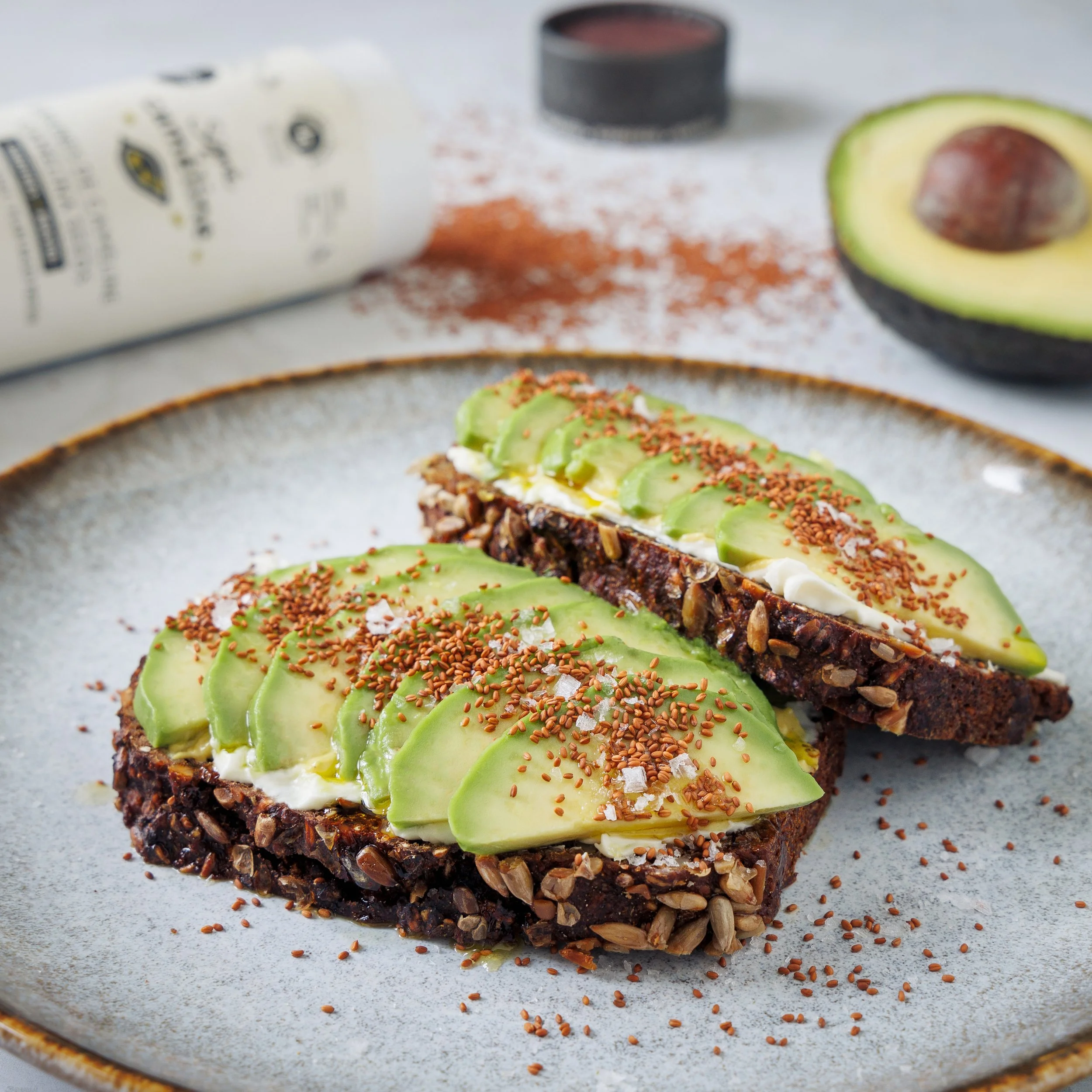 Open-faced avocado toast with seeds, salt, and spices on a ceramic plate.
