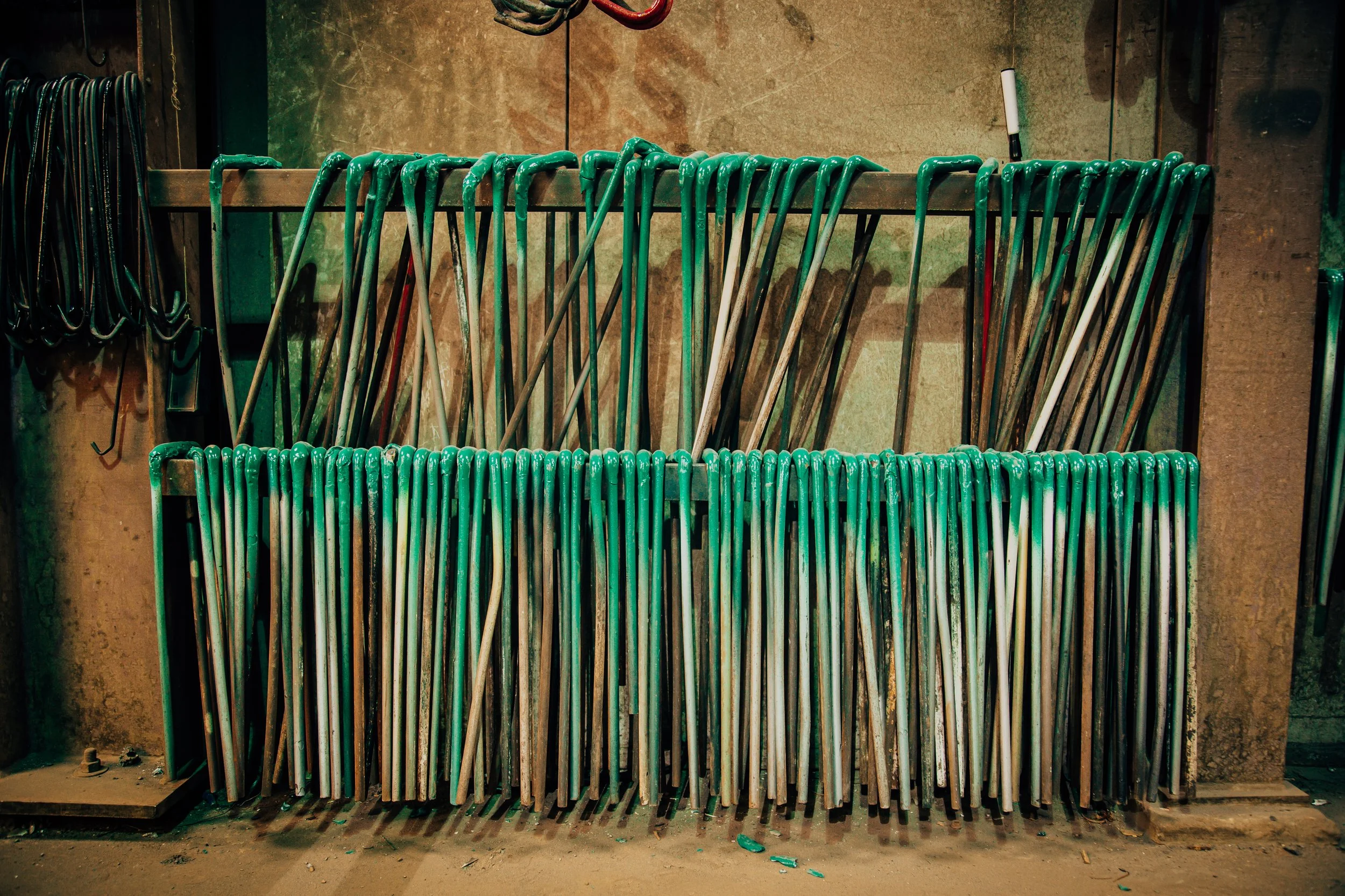 A collection of yard or golf clubs with green grips, stored vertically in an organized rack against a wall.