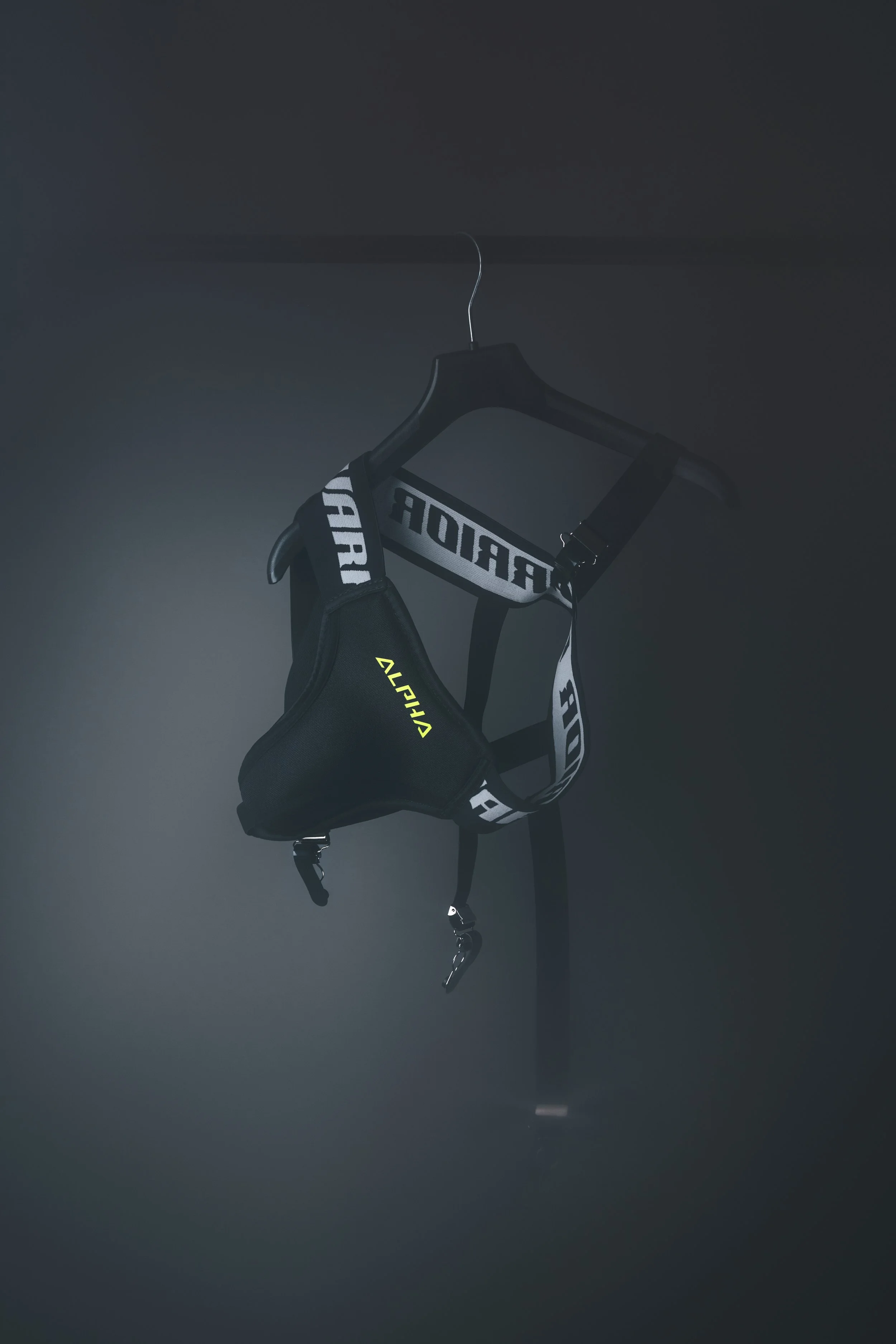 A black jockstrap with white lettering hanging on a black hanger from a dark ceiling.