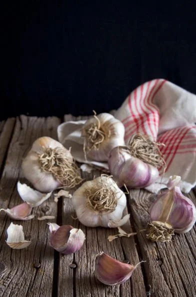 Several heads and cloves of garlic spilled on a rustic wooden surface with a garlic cloth in the background.