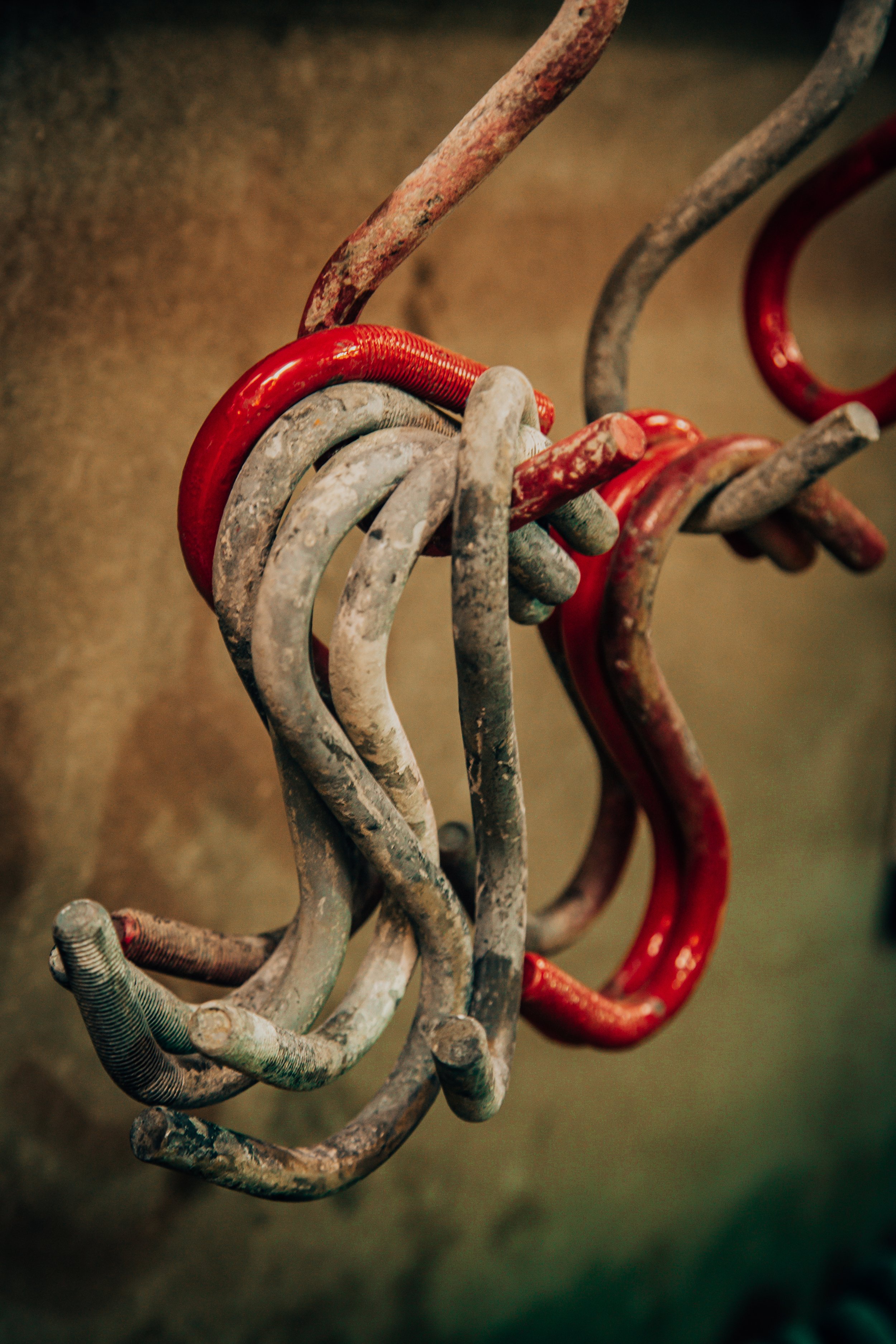 Close-up of intertwined, weathered metal rings, some painted red, set against a blurred, brownish background.