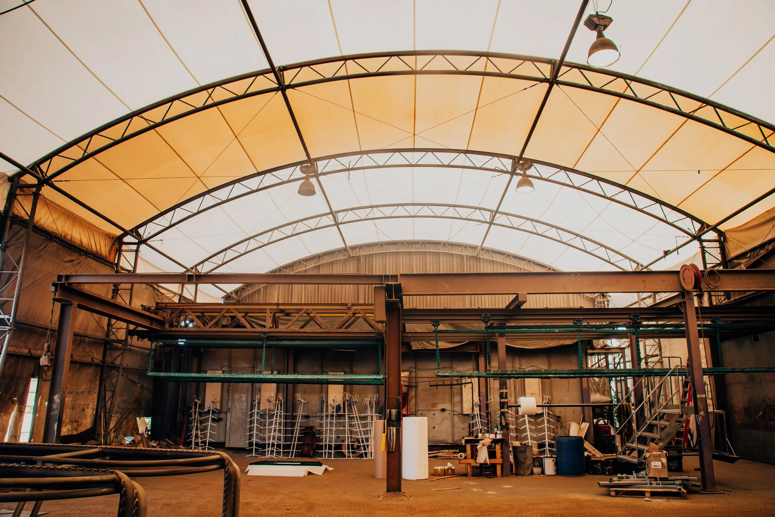 Indoor sports facility or gym under construction with partially completed roof structure, support beams, light fixtures, and some equipment and materials on the floor.