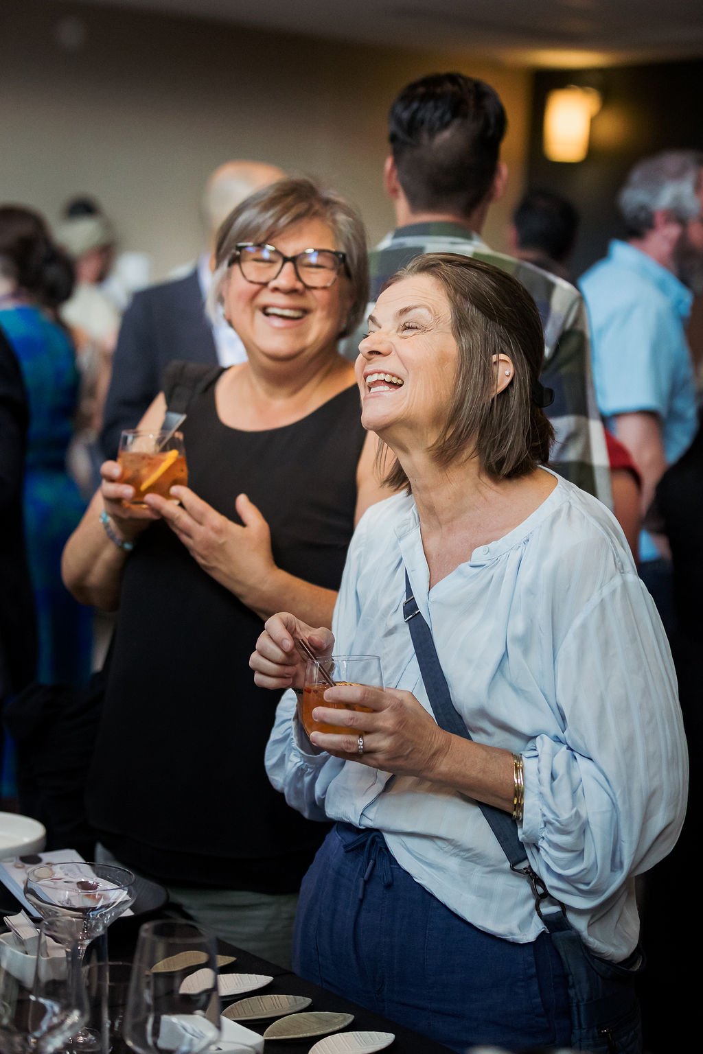 Two women laughing and enjoying drinks at a social event or party
