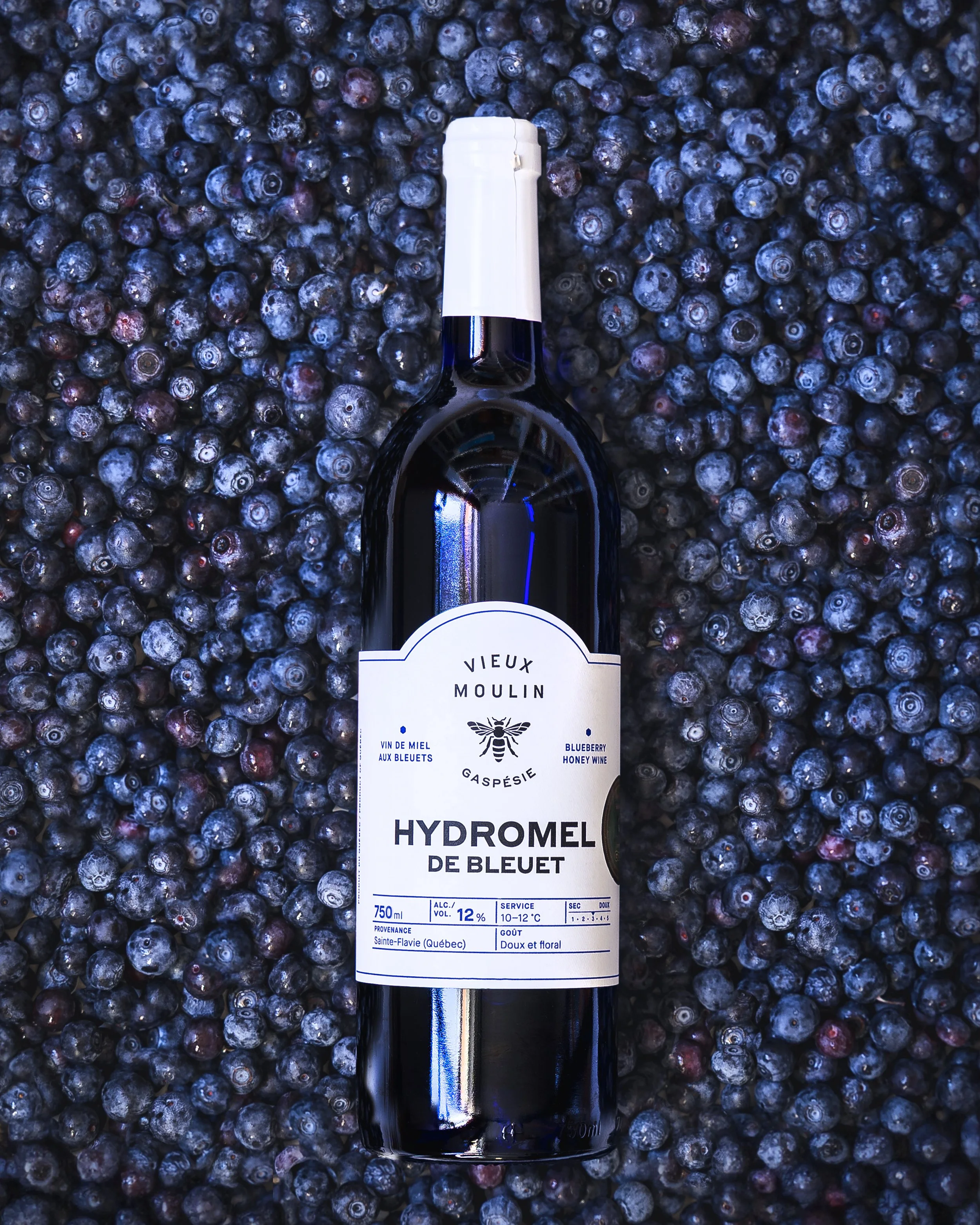 A bottled beverage resting on a bed of blueberries.