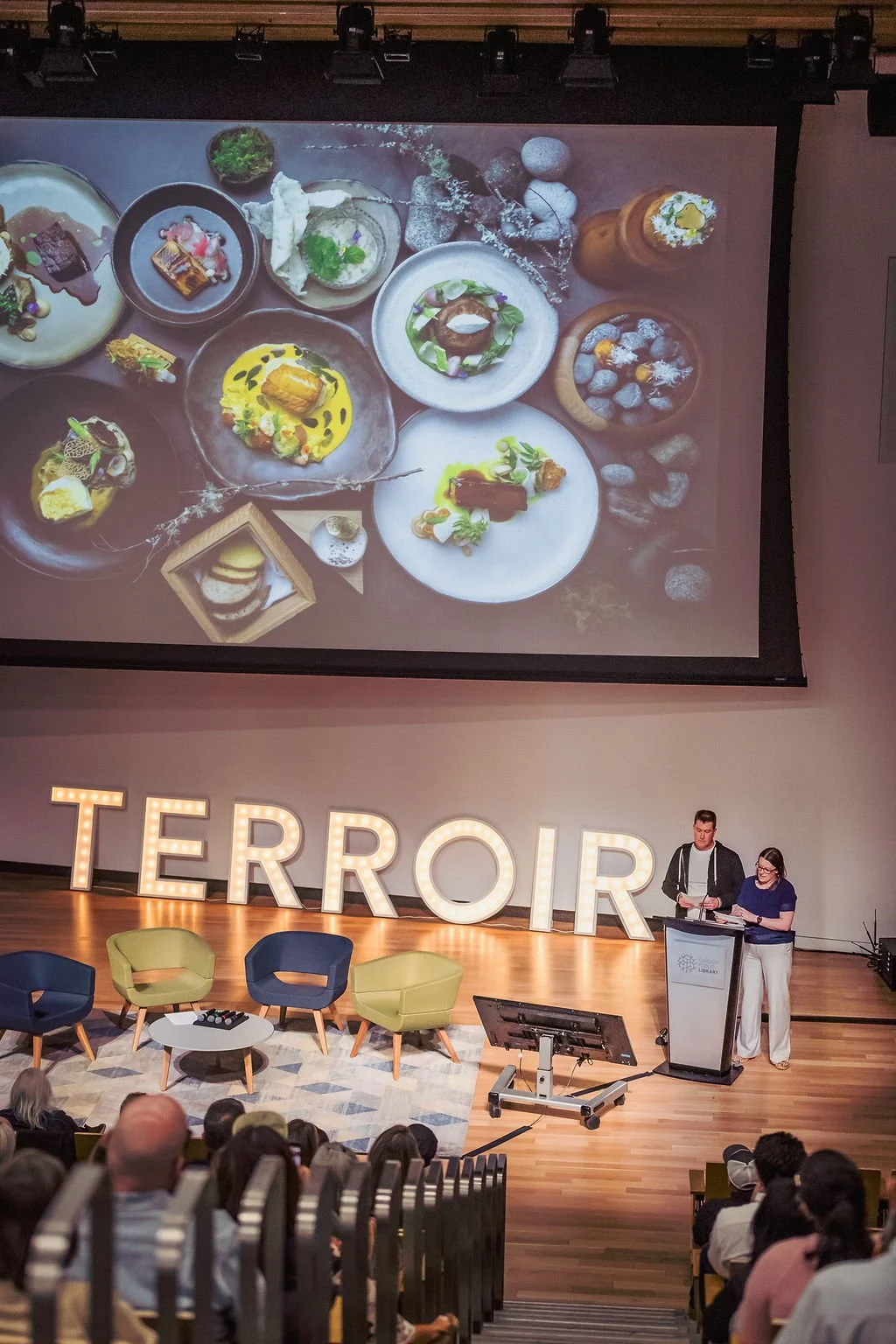 A large screen displaying a variety of artistic, colorful dishes in a presentation or exhibition setting, with the word 'TERROR' lit up in large illuminated letters on the stage below.