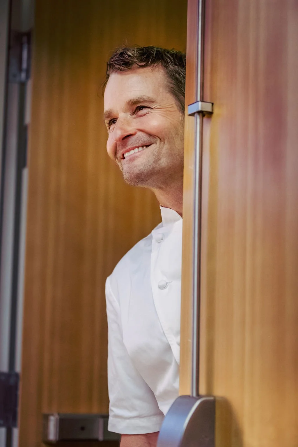 Chef smiling and peeking out from behind a wooden kitchen cabinet.