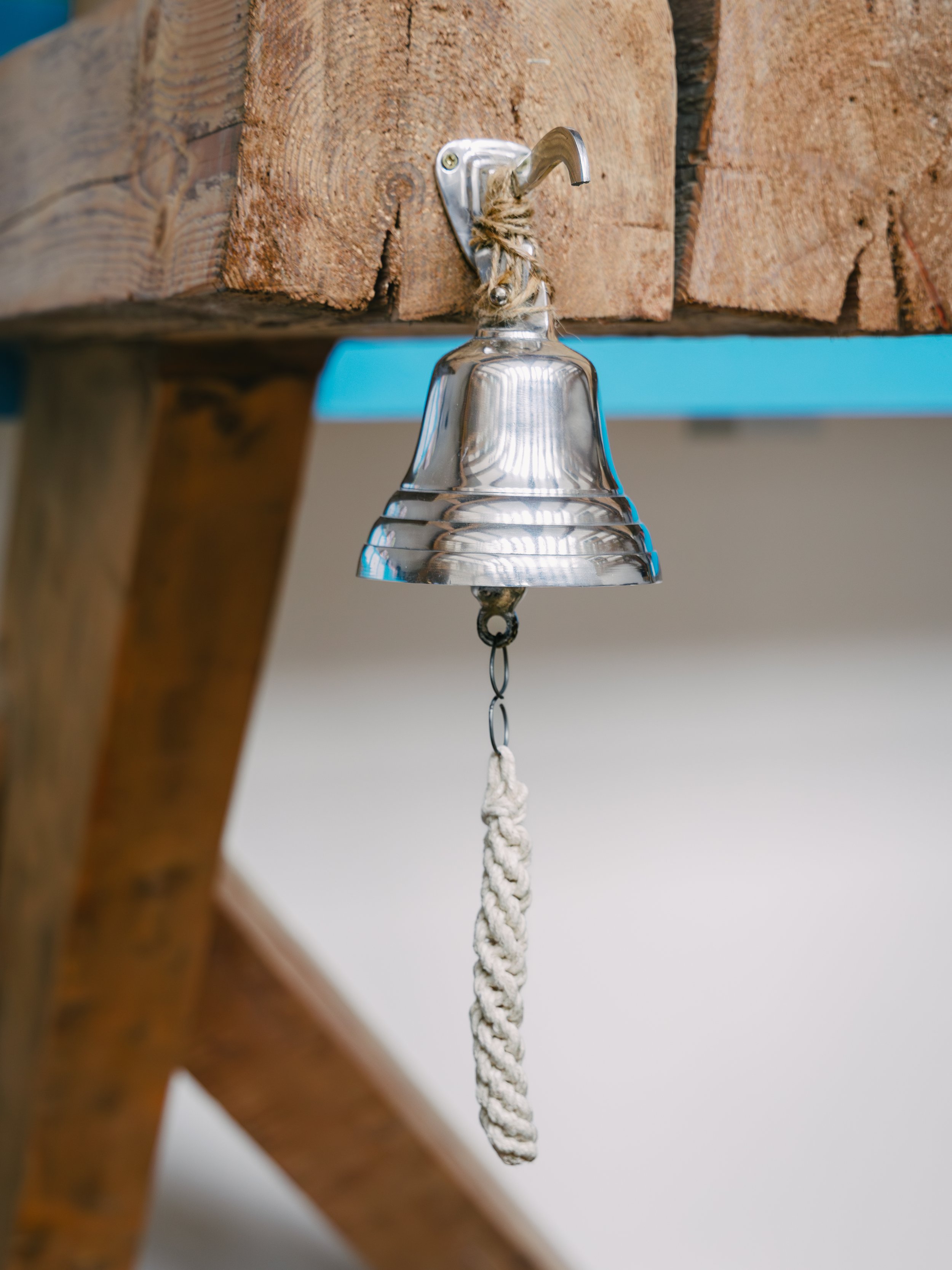 A metal bell hanging from a wooden beam with a rope attached to its clapper.