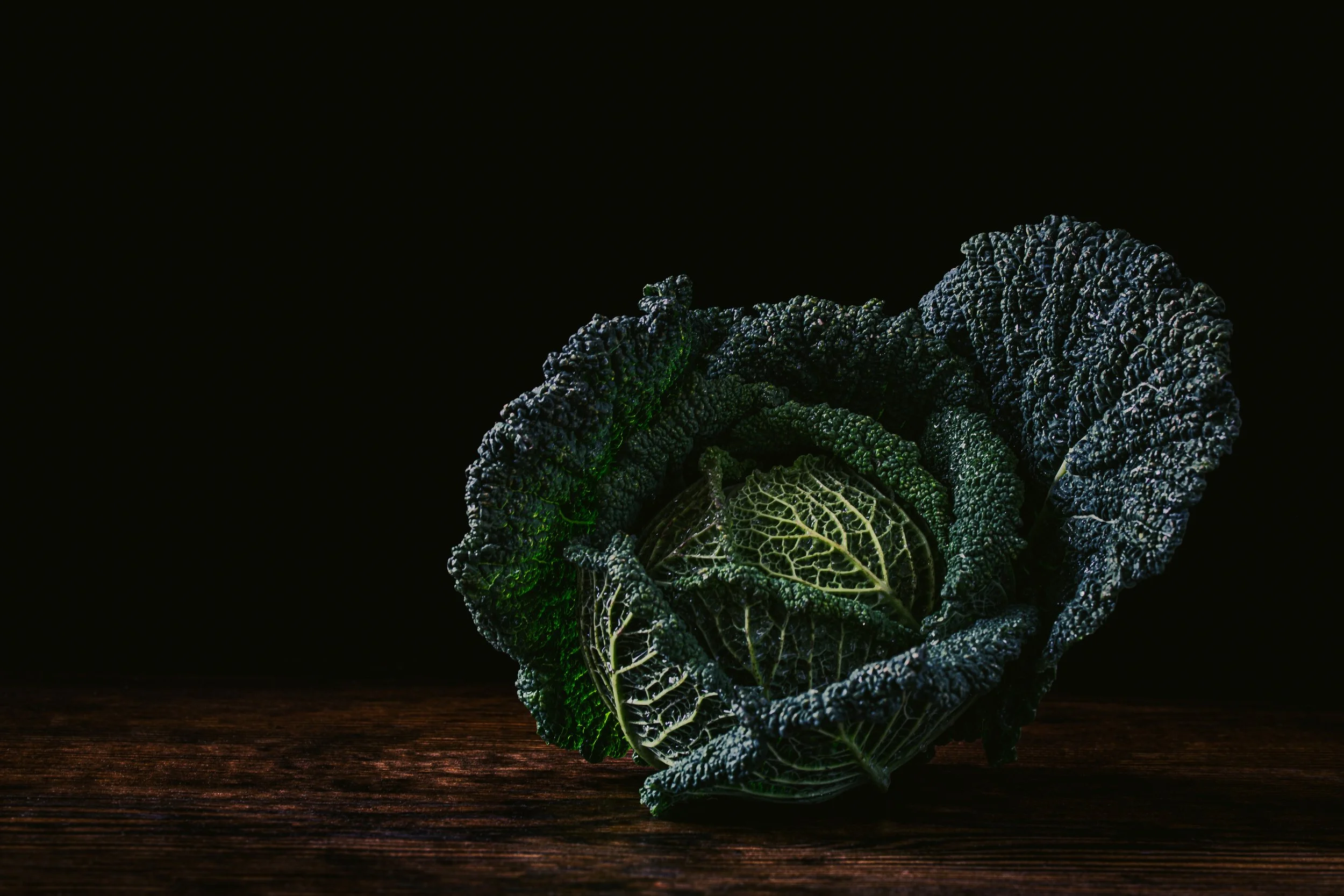 Fresh kale leaves on a dark wooden surface with black background.