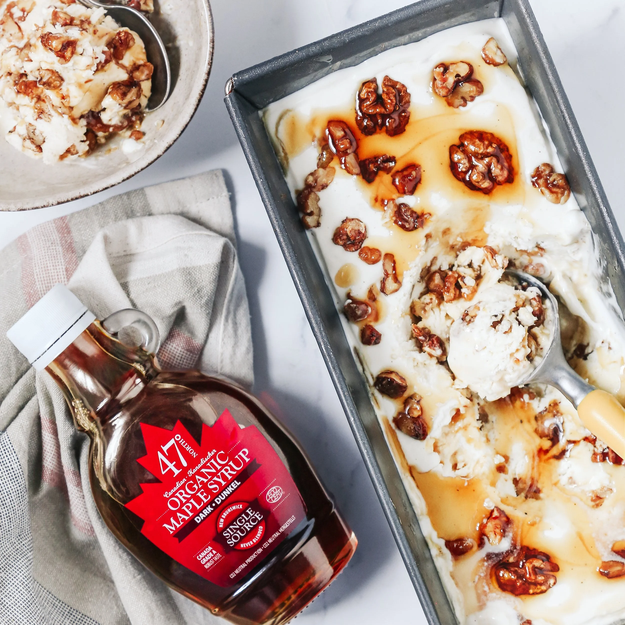 A bottle of Ontario maple syrup next to a tray of ice cream topped with chopped nuts and caramel syrup.