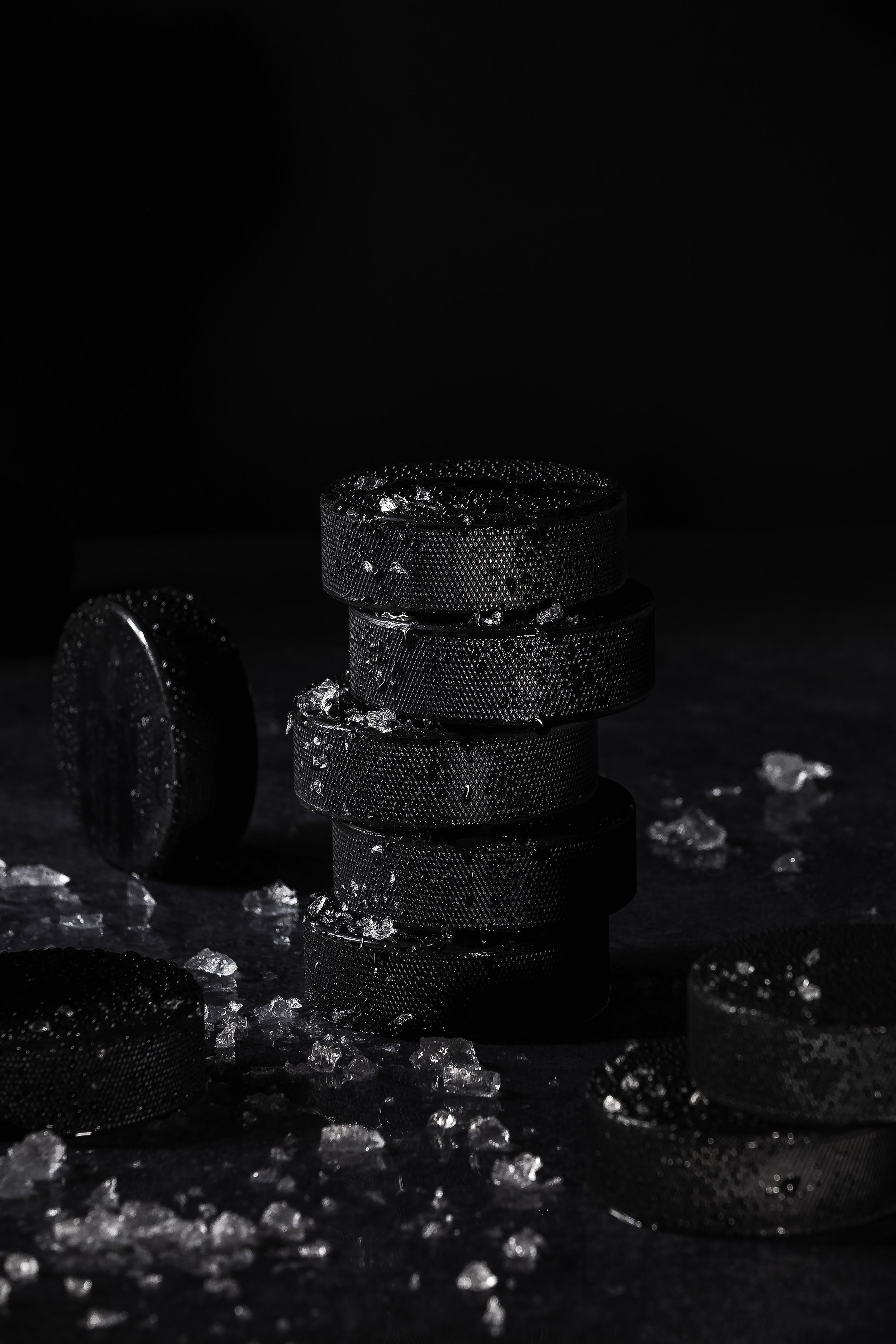 Stacked hockey pucks with crushed ice scattered around them on a dark surface.