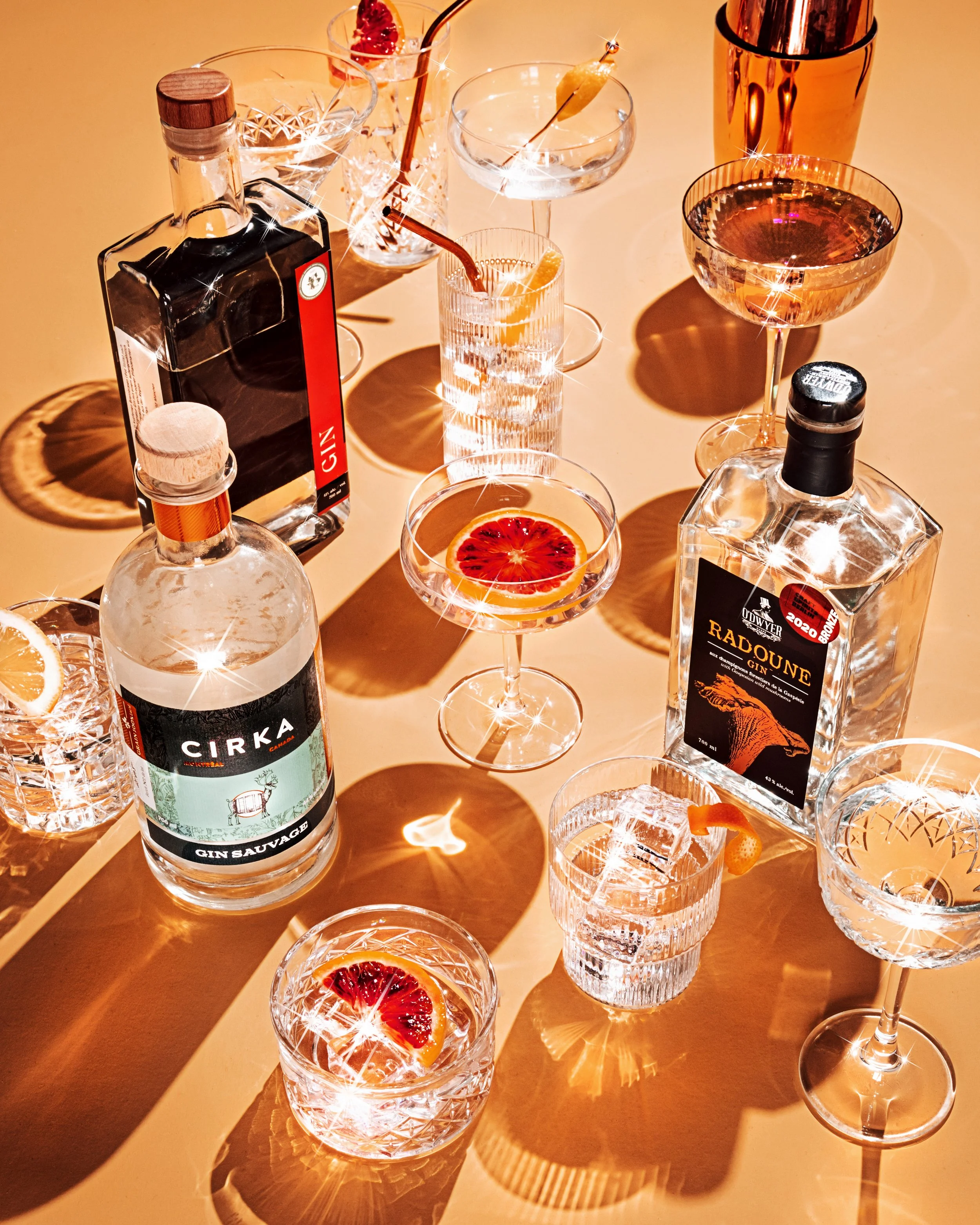An assortment of cocktails and bottled alcohol on a table, garnished with fruit slices, with shining reflections and shadows.