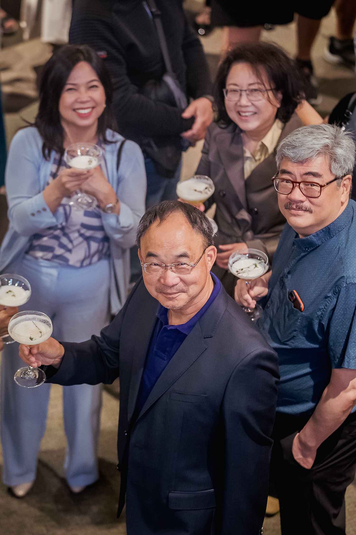 A group of people enjoying a social gathering, holding glasses of drinks, smiling, dressed in semi-formal attire.