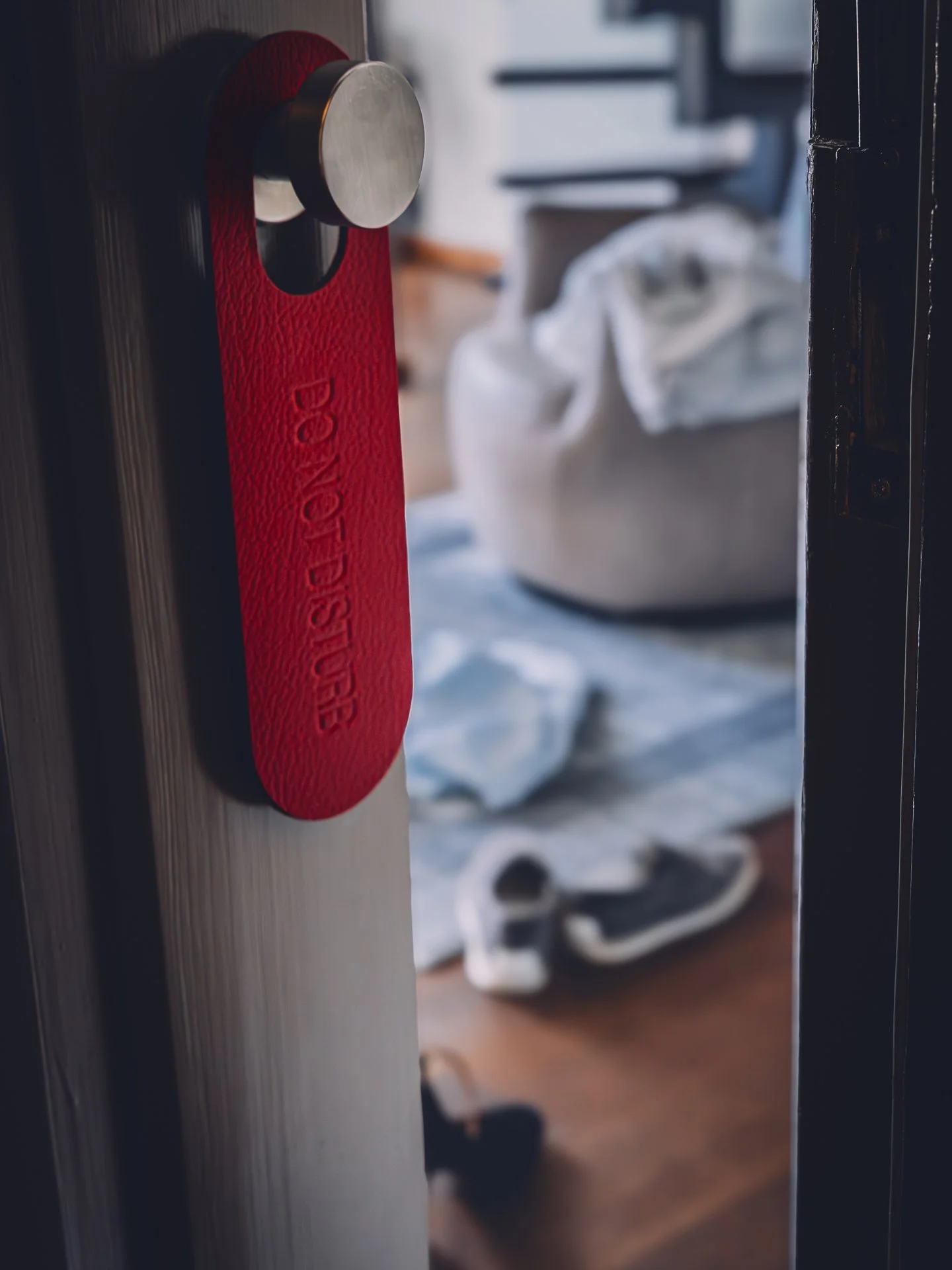 Door with a red caution sign and a round metallic handle, with a laundry basket and scattered items in the background.