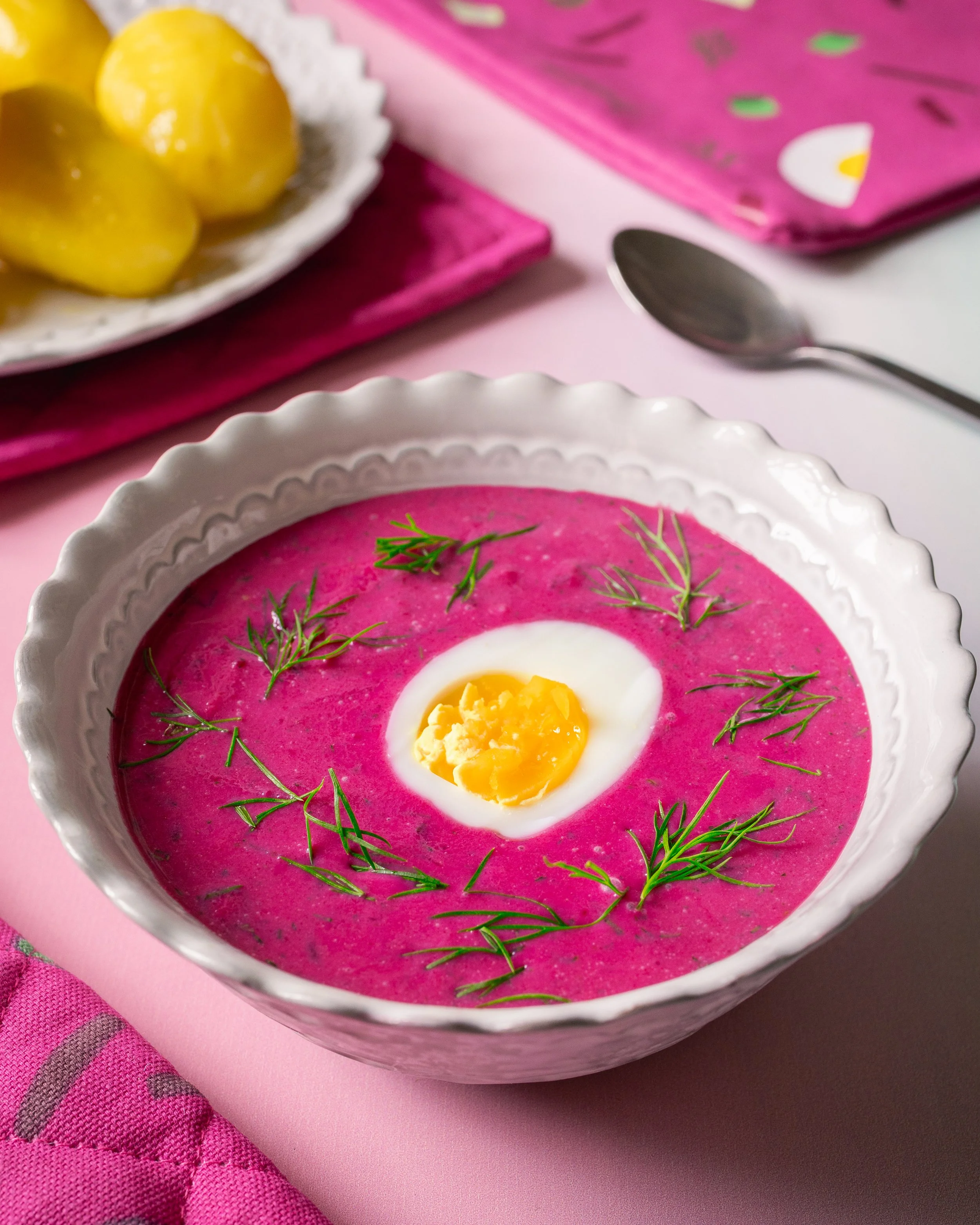 A bowl of cold beet soup garnished with dill and a halved boiled egg.