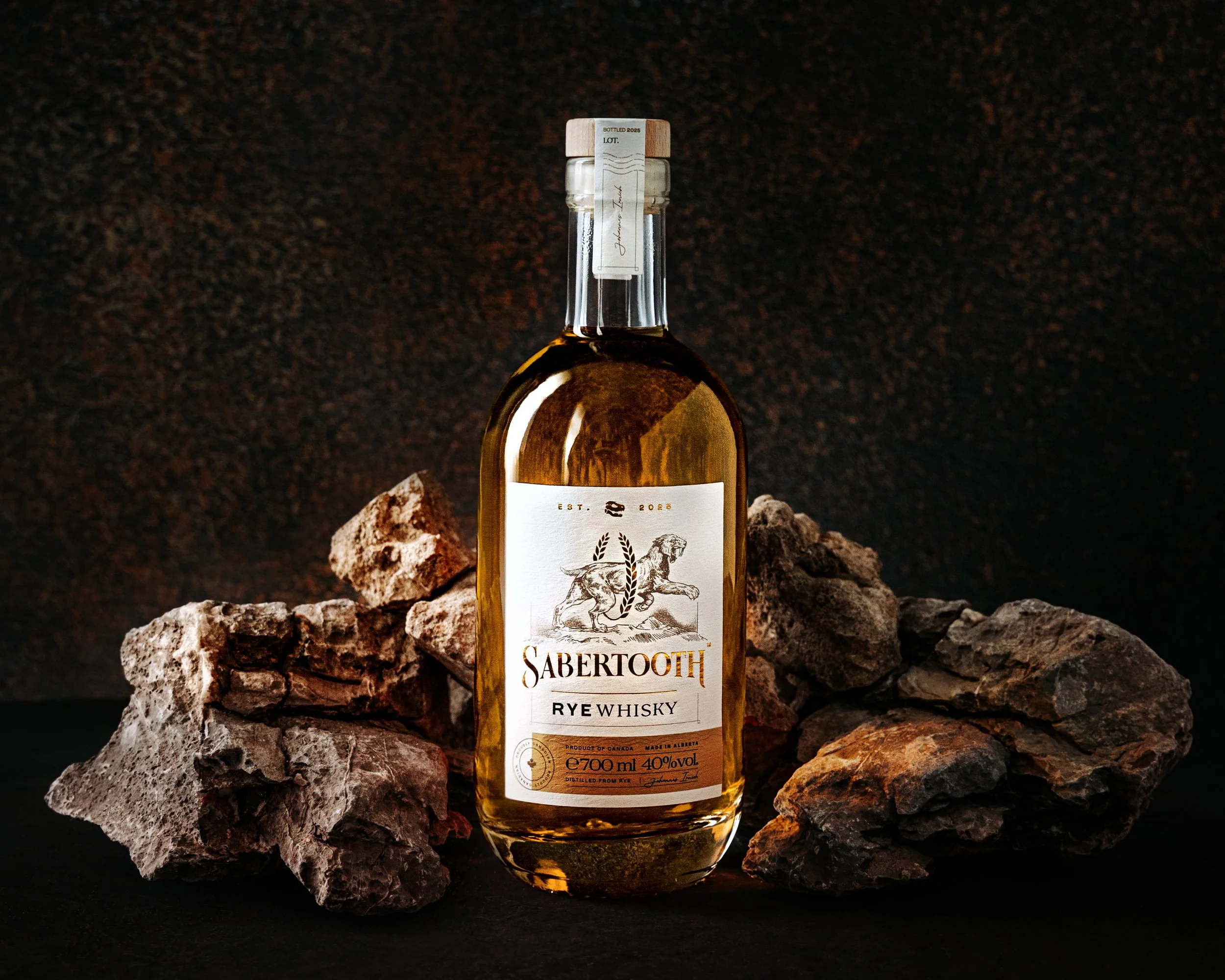 A bottle of Sabertooth Rye Whisky placed on rocks against a dark background.