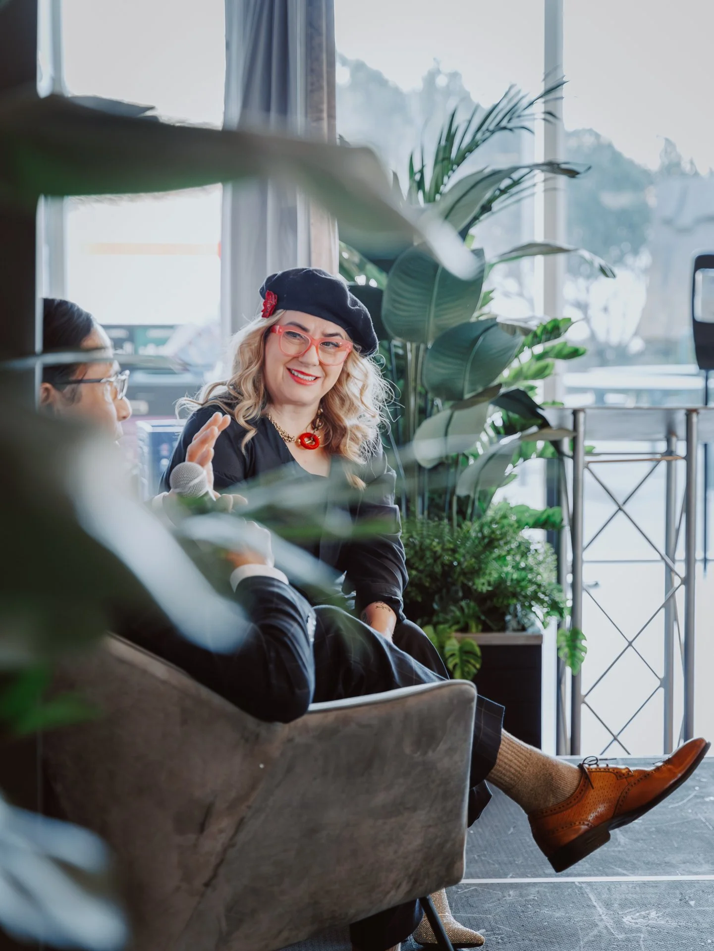 People sitting on couches in a bright, plant-filled room, engaging in conversation.