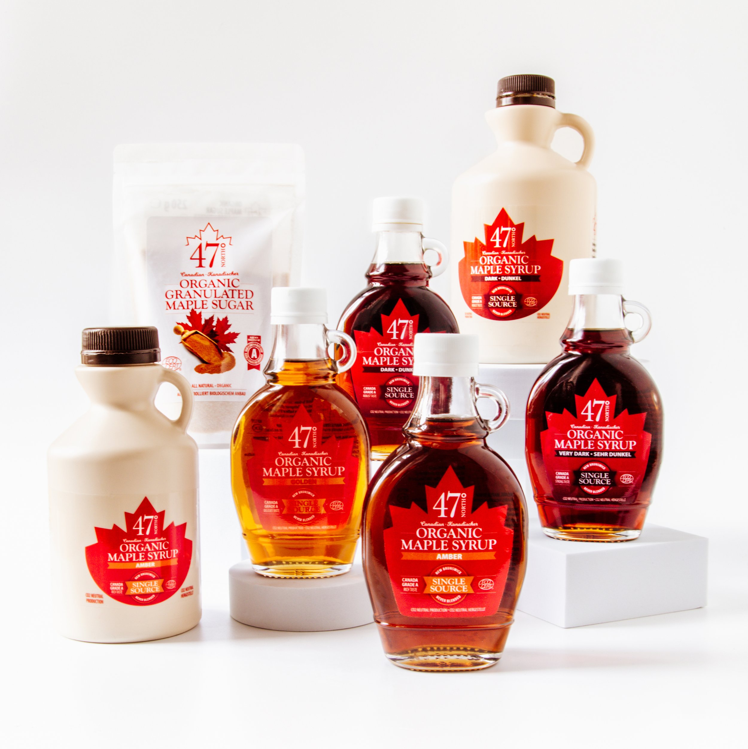 Collection of maple syrup bottles and containers, including organic maple syrup in glass bottles and a white jug, placed on a white background.