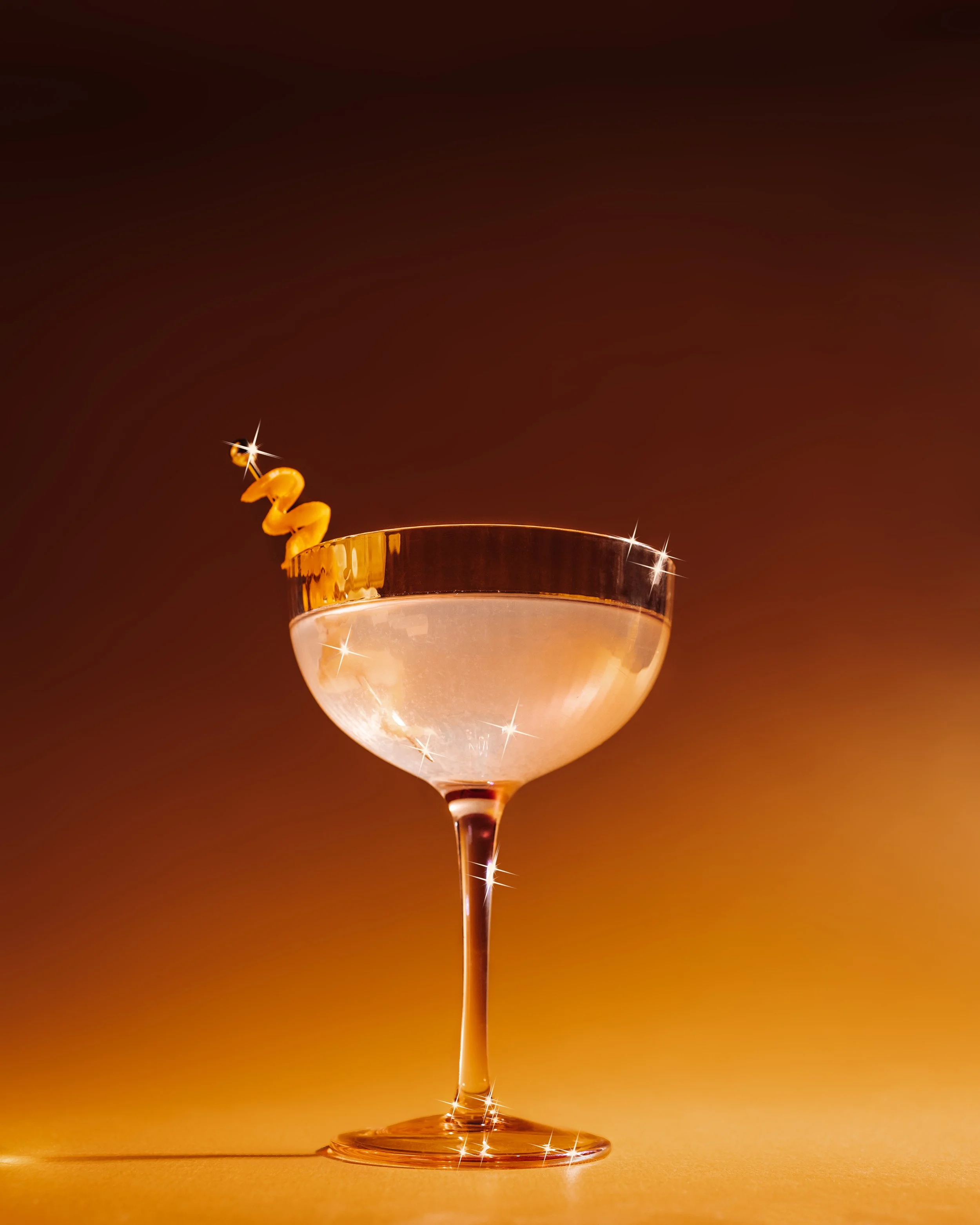 A close-up of a champagne glass with a spiraled yellow decoration on the rim and a dark background with a warm gradient.