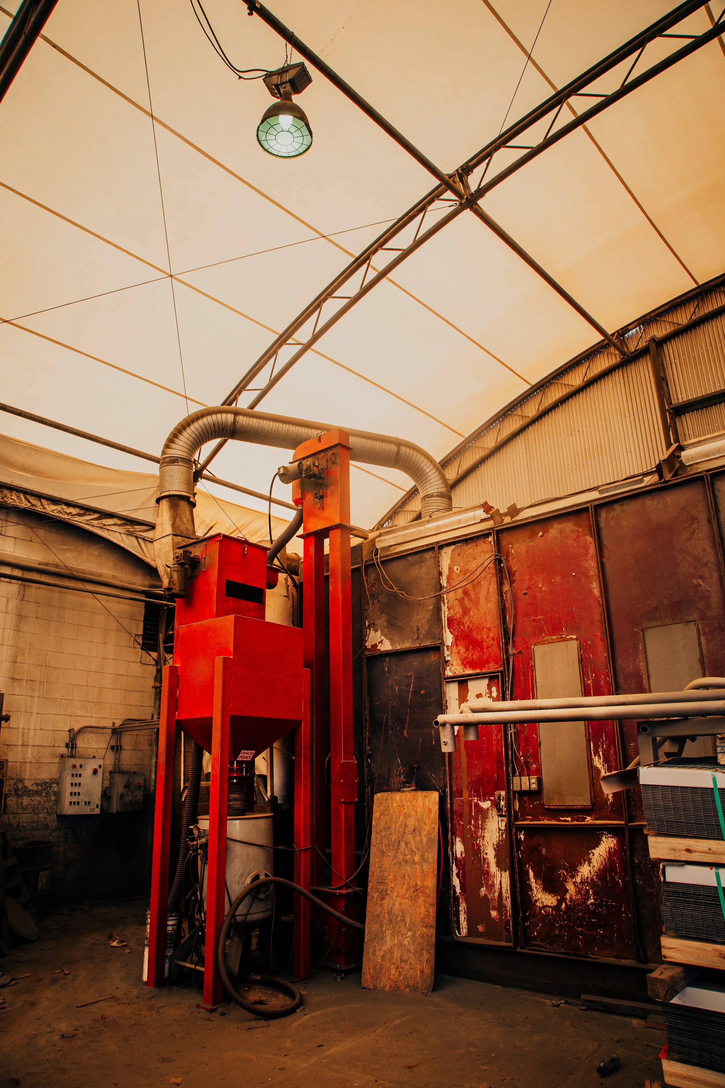 Industrial workshop with a green overhead light, red machinery, ducts, and rusted metal walls.
