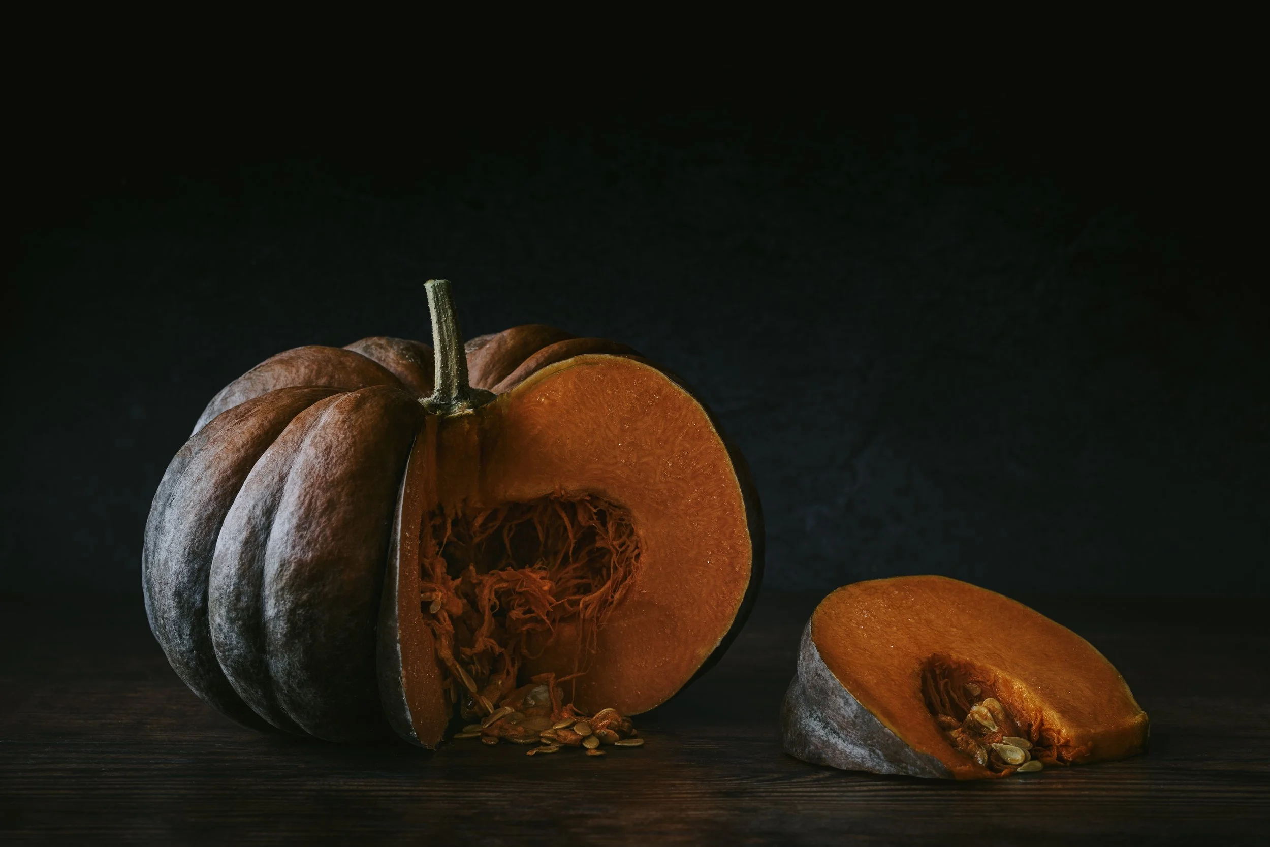 Whole and sliced pumpkin on a dark surface with a black background.