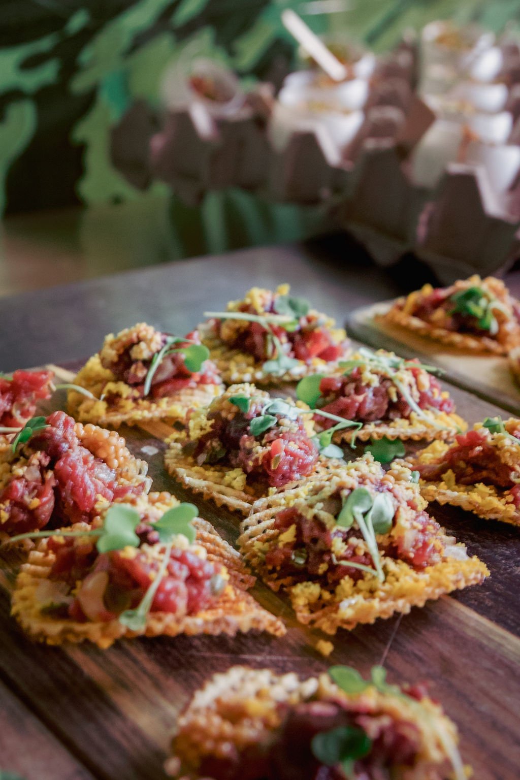 Close-up of crispy taco slices topped with seasoned meat, diced tomatoes, and microgreens on a wooden serving board.