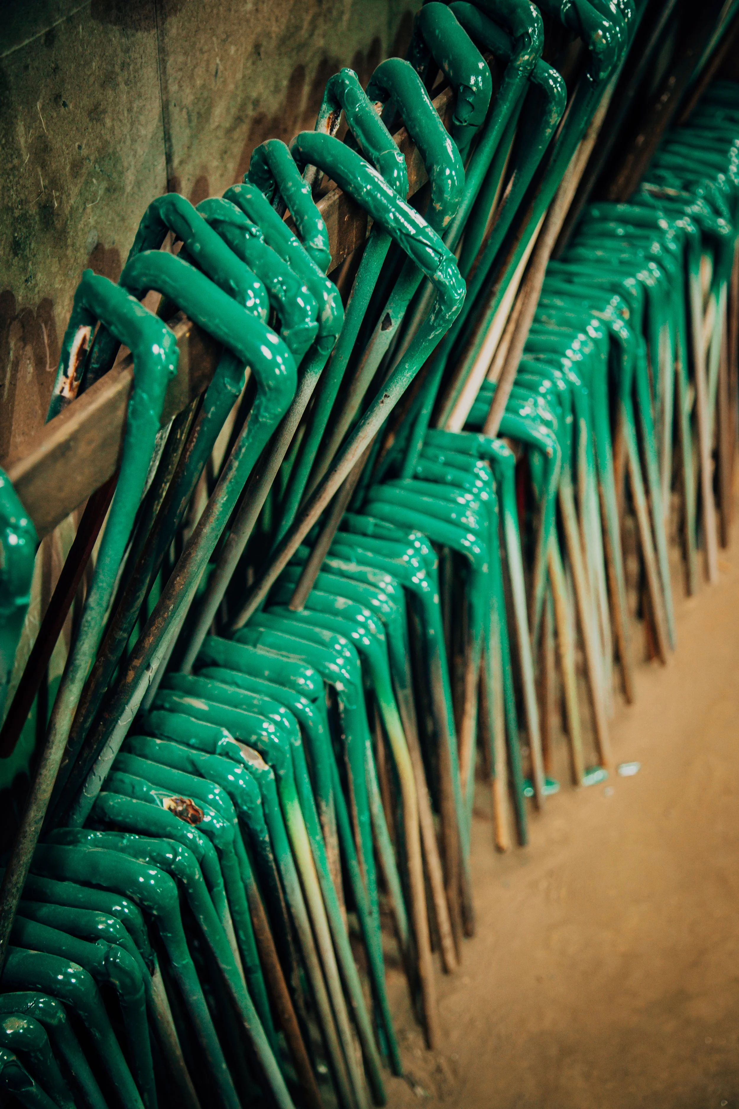 Green metal chairs with chipped paint are stacked against a wall in a row.