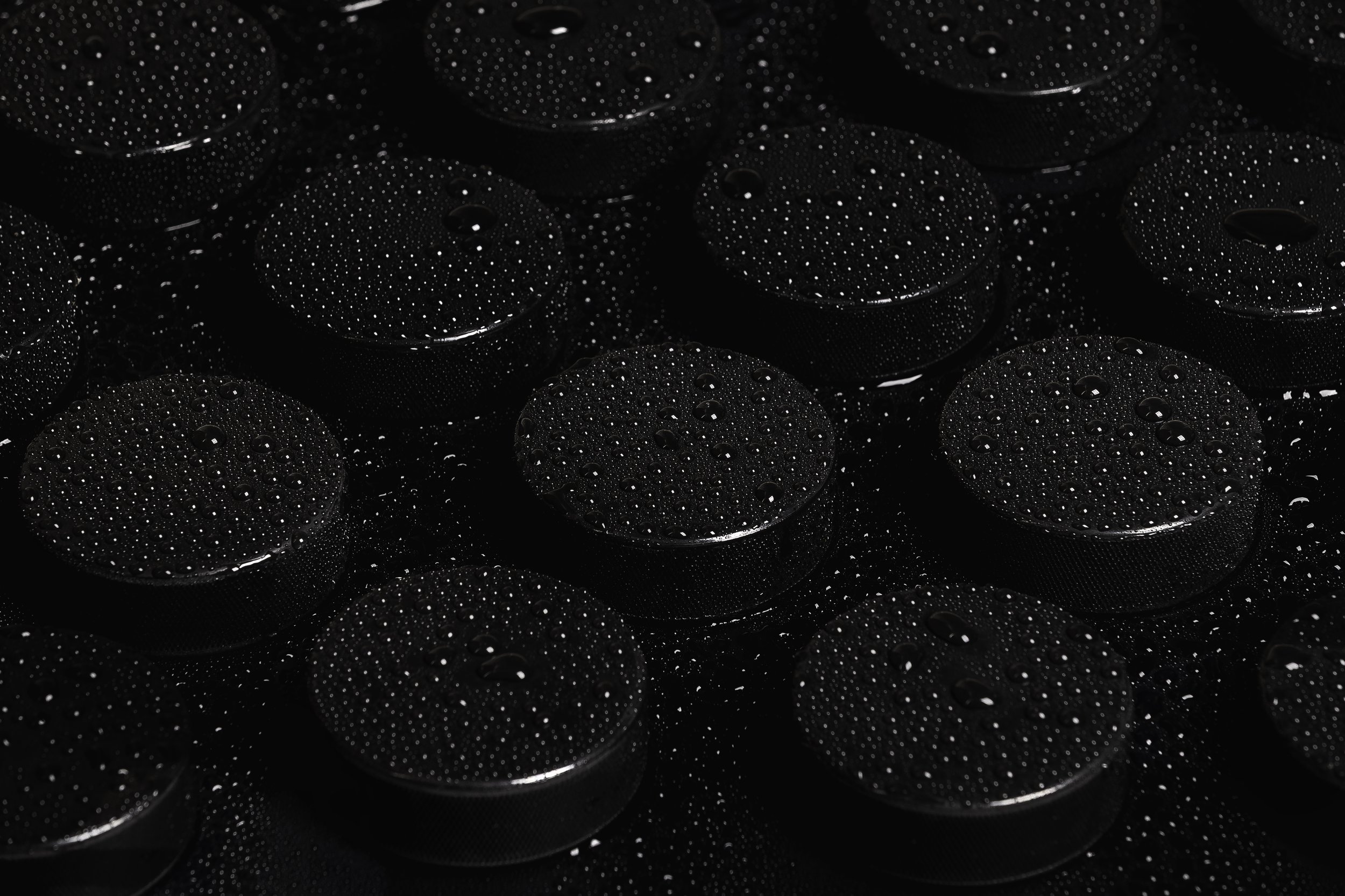 Close-up of black hockey pucks covered in tiny water droplets on a dark surface.