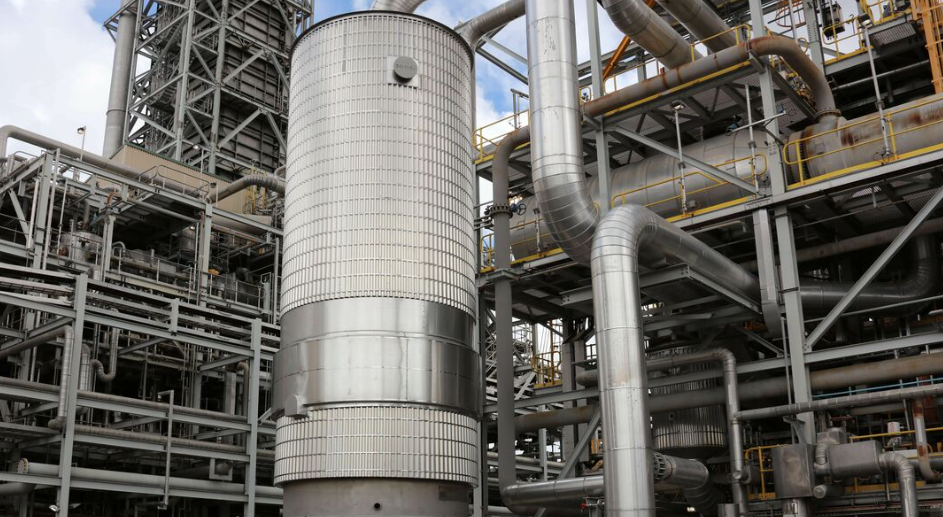Industrial facility with large metal pipes, a tall cylindrical structure, and metal framework.
