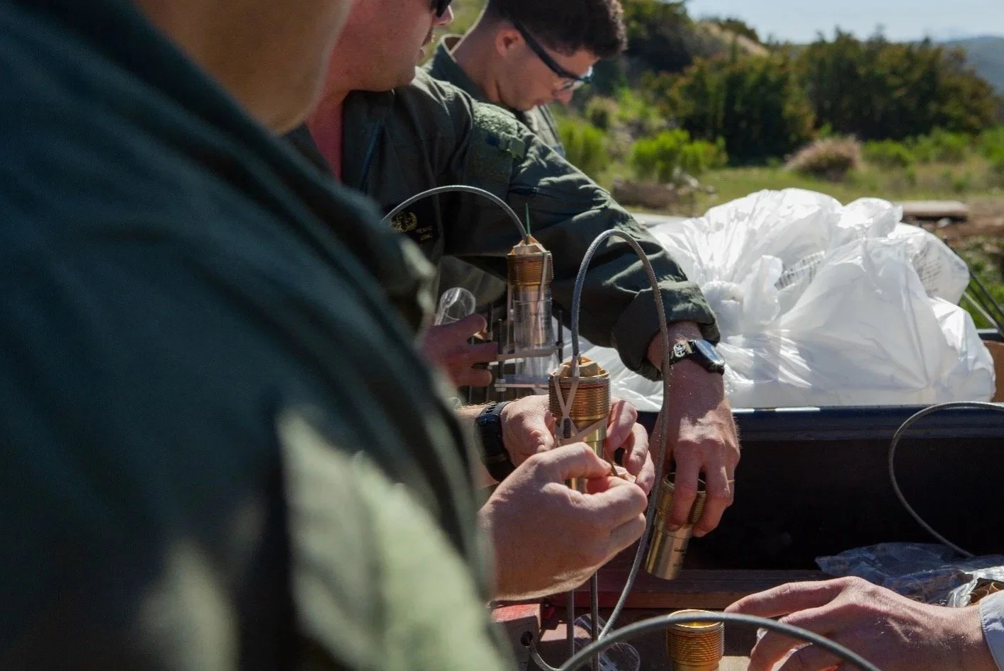 Scientists working outdoors with small, intricate electronic devices and wires, possibly conducting a scientific experiment.