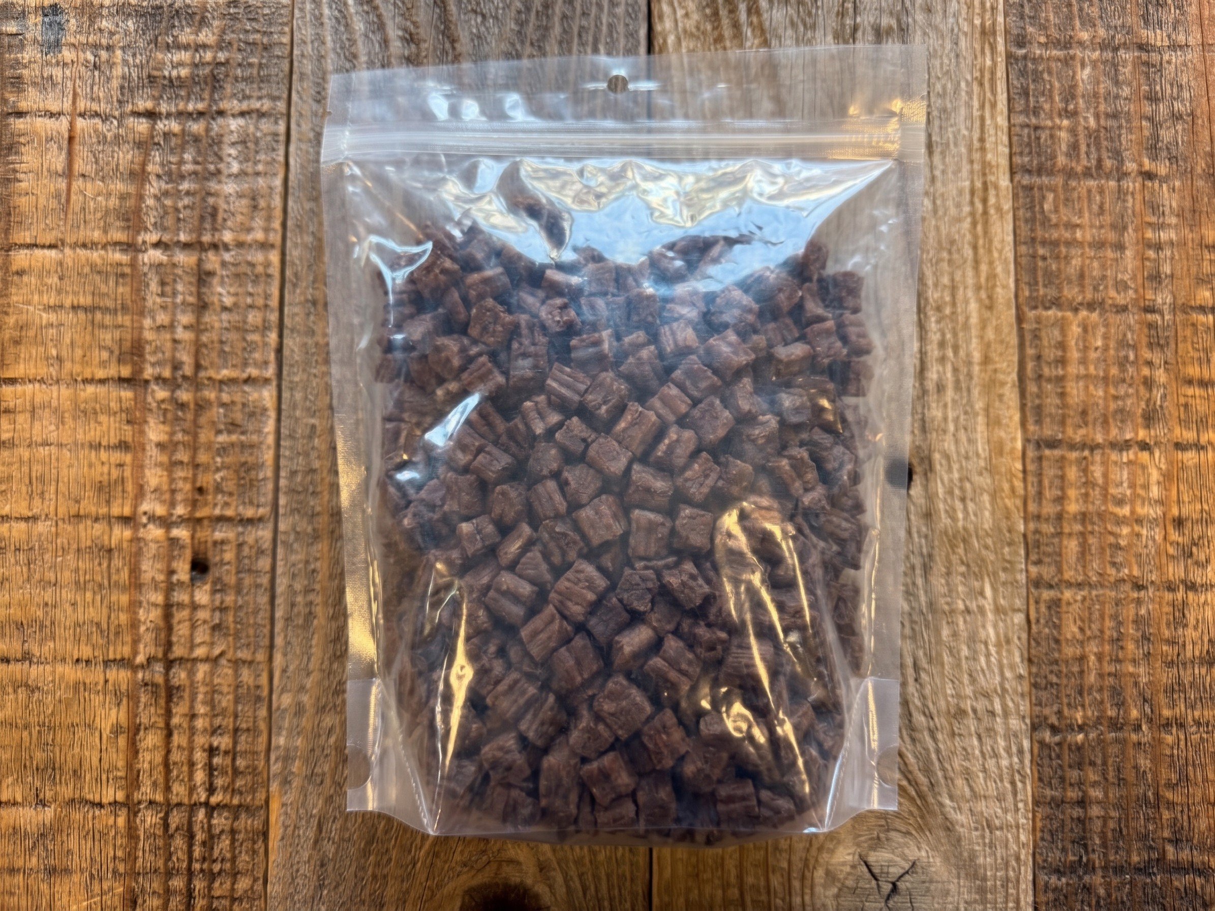 Clear resealable bag filled with small beef treats on a rustic wooden surface