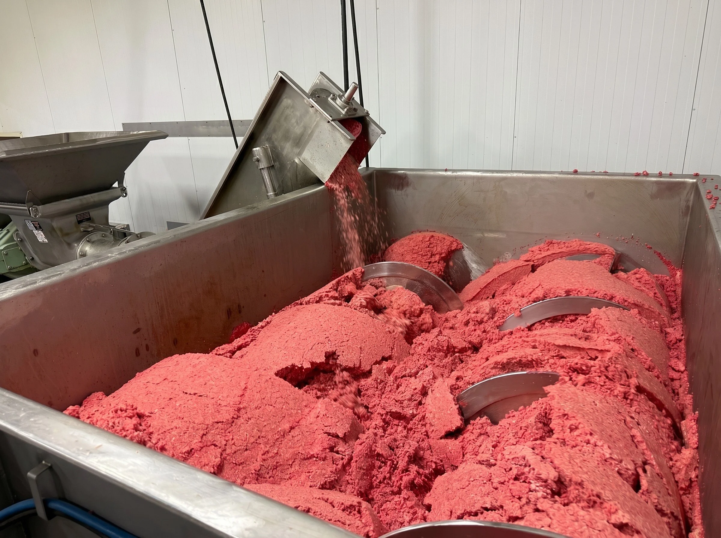 Industrial stainless steel mixer processing ground red meat in a food production facility
