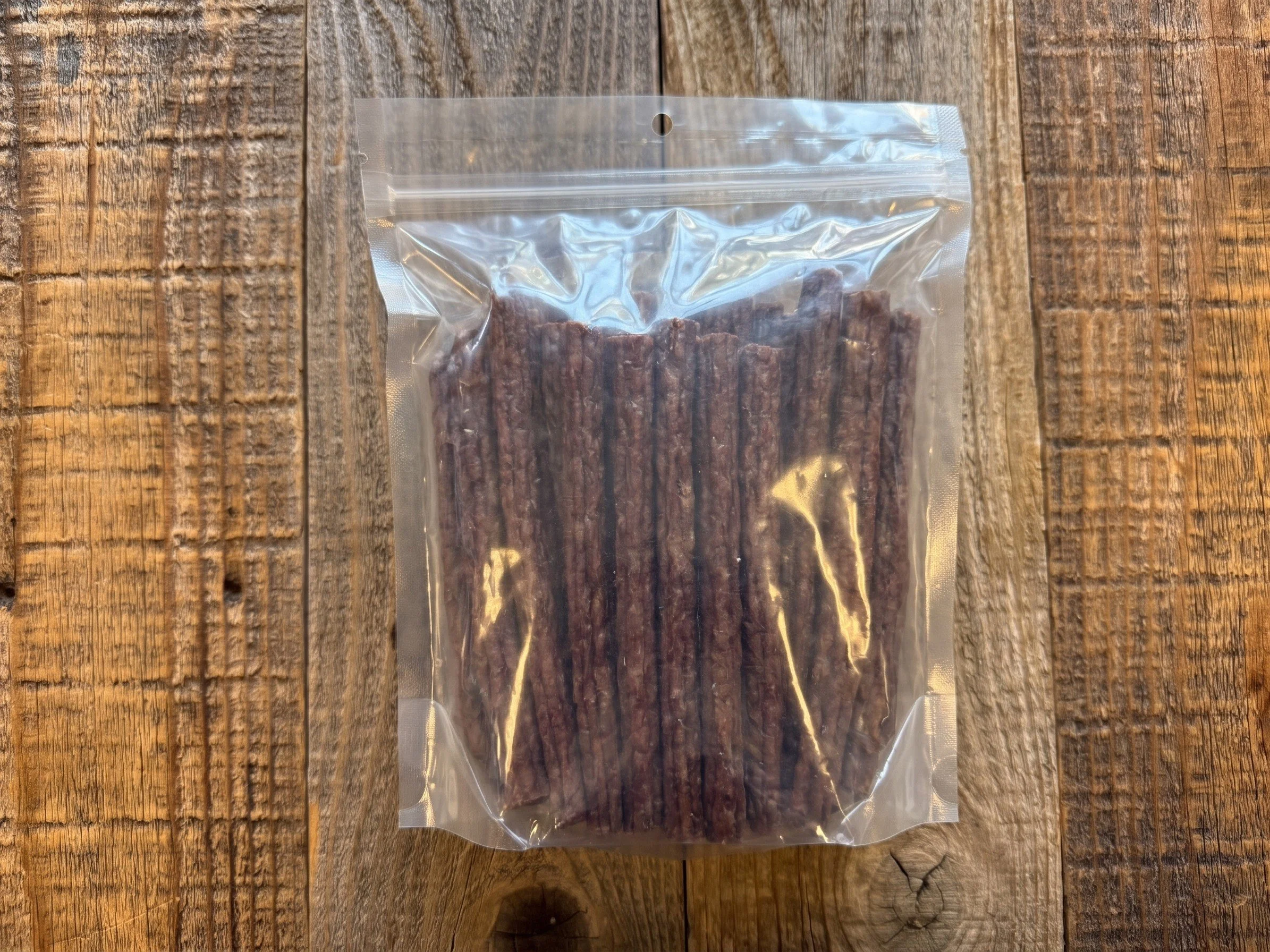 Clear resealable bag of dark brown beef jerky sticks on a rustic wooden table