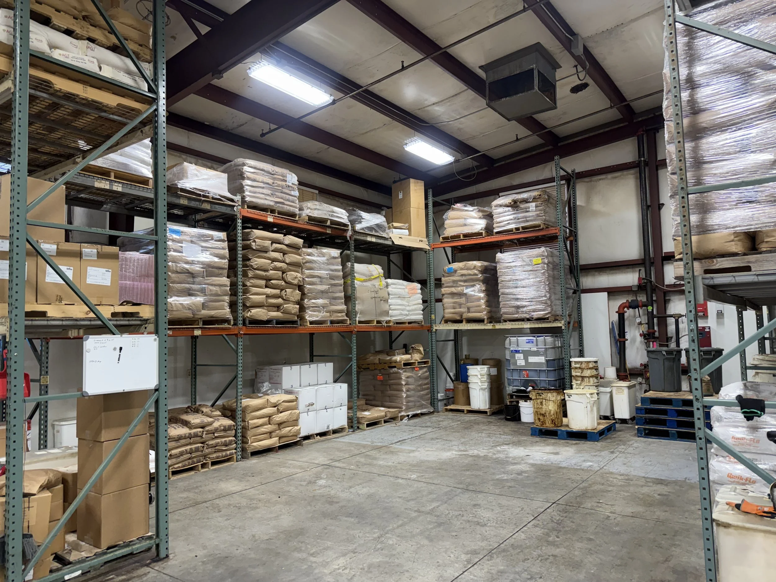 Industrial warehouse with pallet racks storing bags, boxes, and containers of bulk materials.