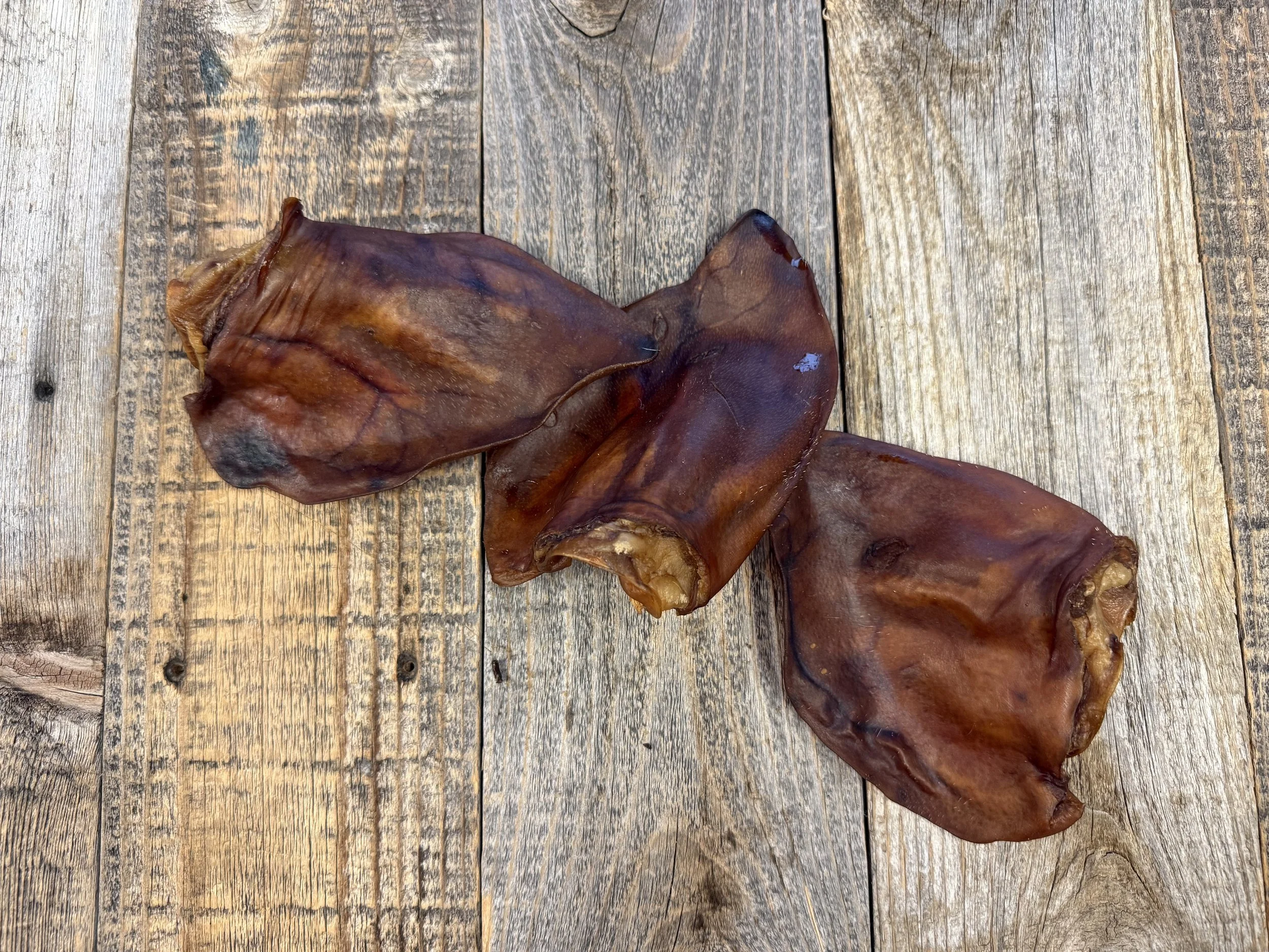 Dried brown pig ears arranged on a rustic wooden surface