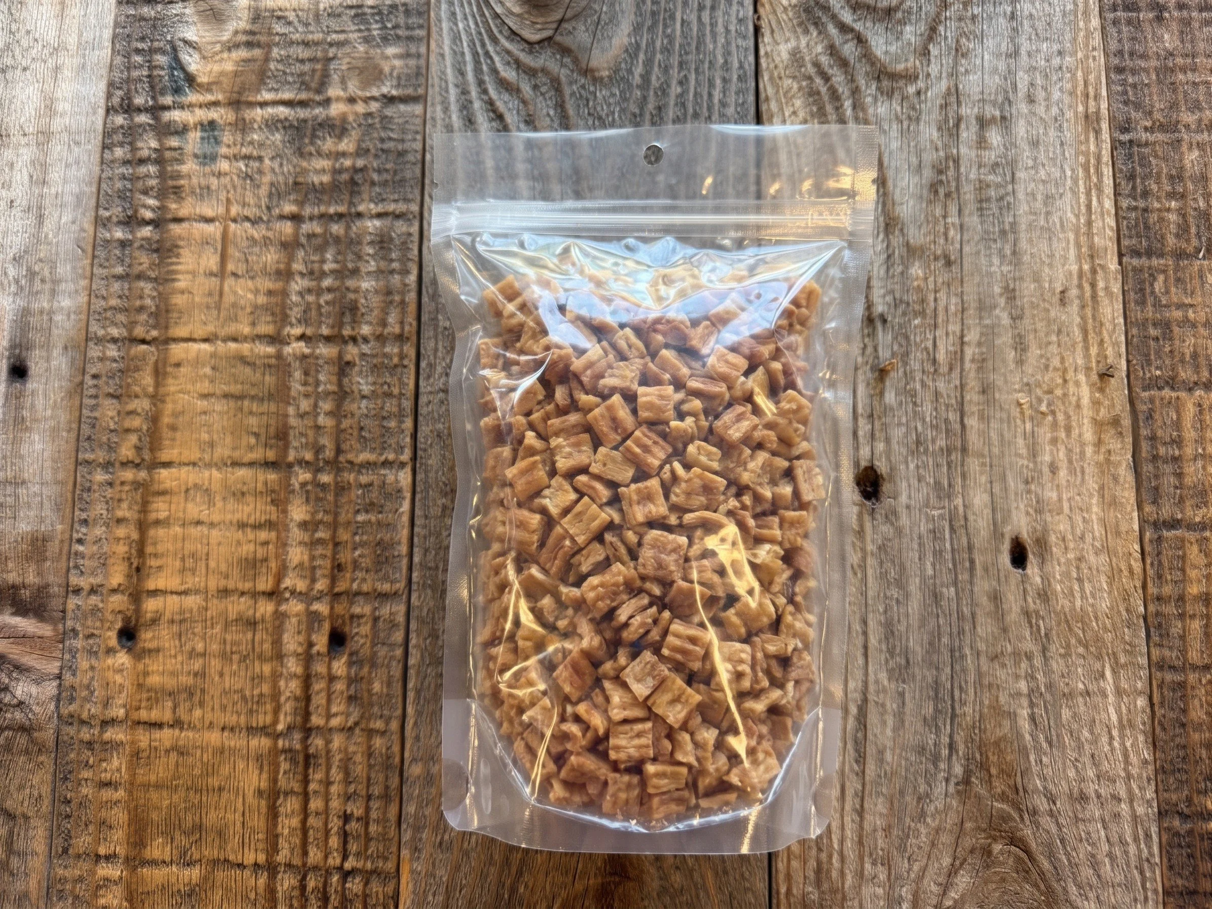 Clear resealable bag filled with small golden-brown dried chicken treats on a rustic wooden table