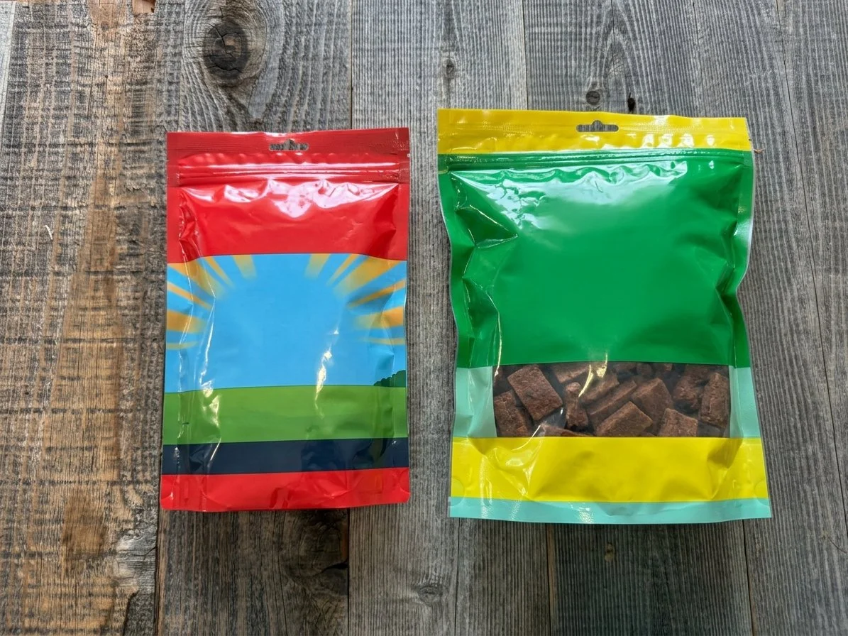 Two colorful resealable snack bags on a rustic wooden table, with brown treats visible inside the green and yellow bag.