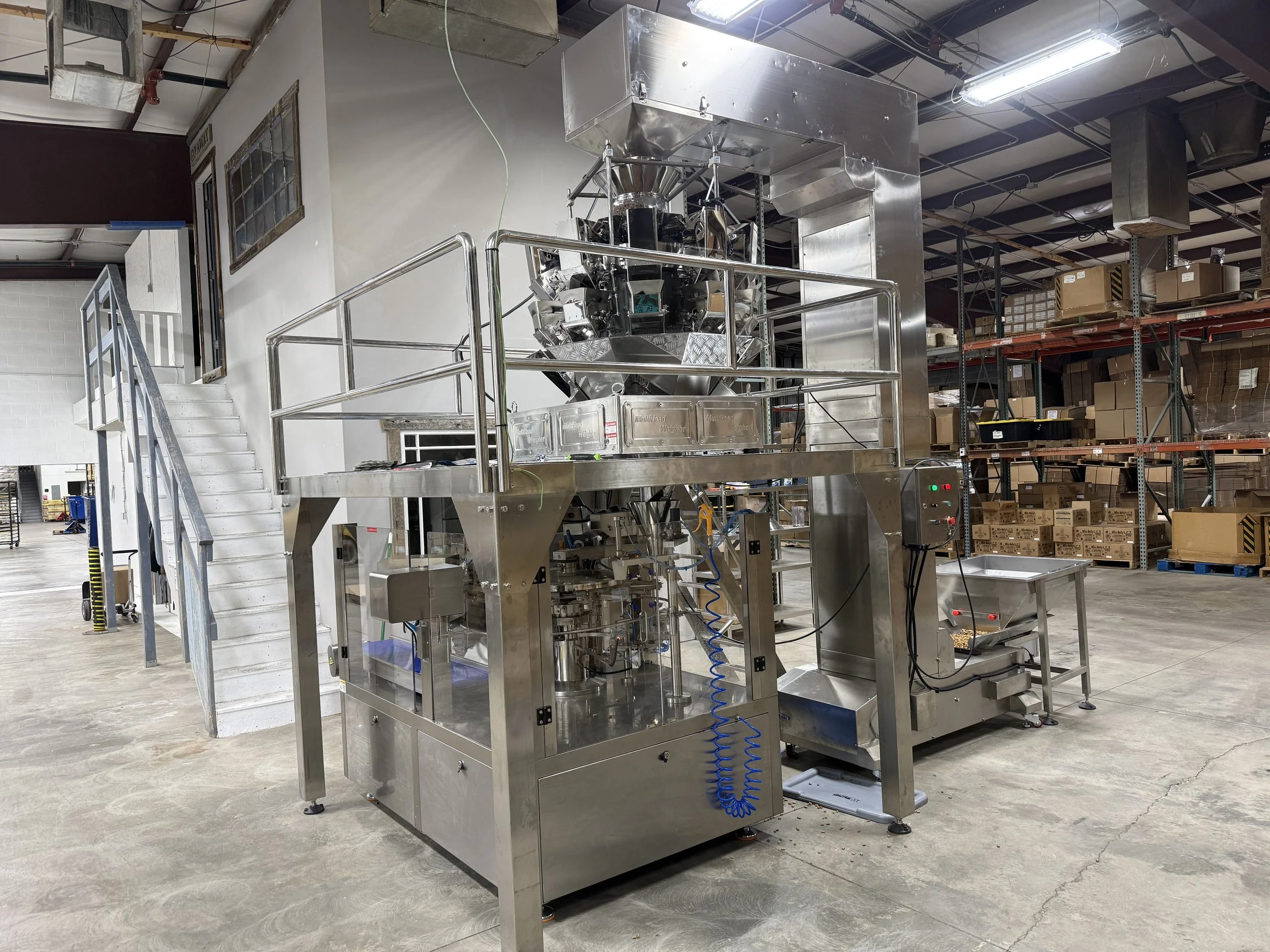Industrial stainless steel food packaging machine with a multihead weigher in a warehouse production facility