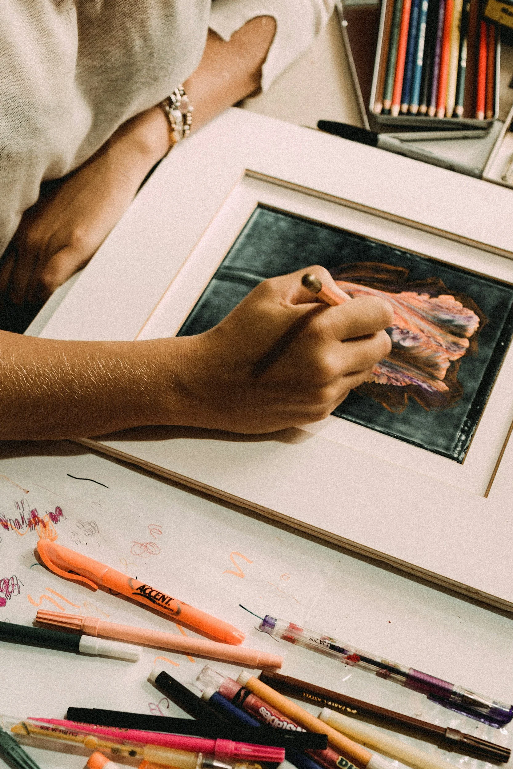 A person drawing and treating a decoupage image , surrounded by additional art supplies and drawings.