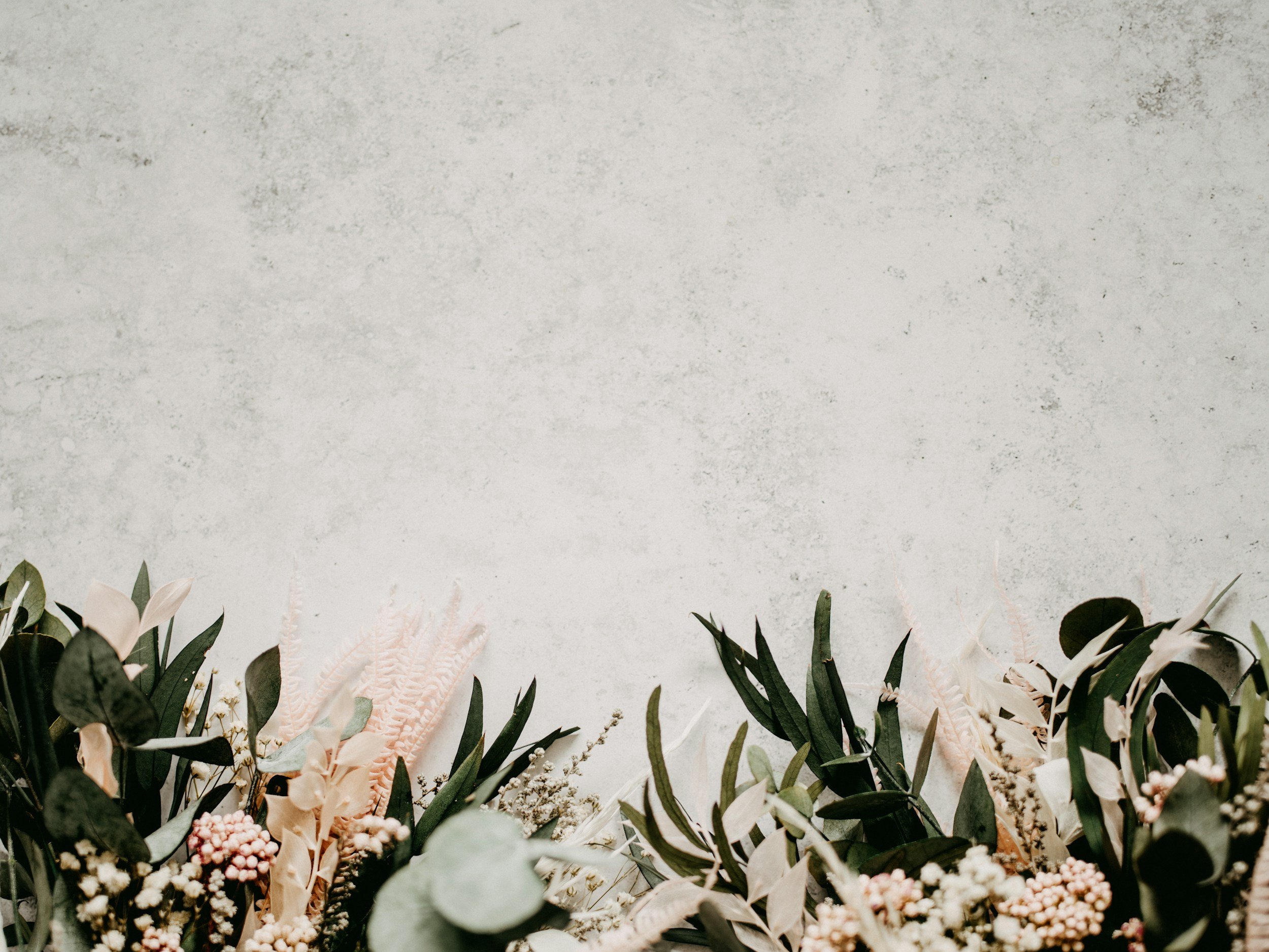 Decorative floral arrangement with green leaves, white and pink flowers, set against a textured light gray wall.
