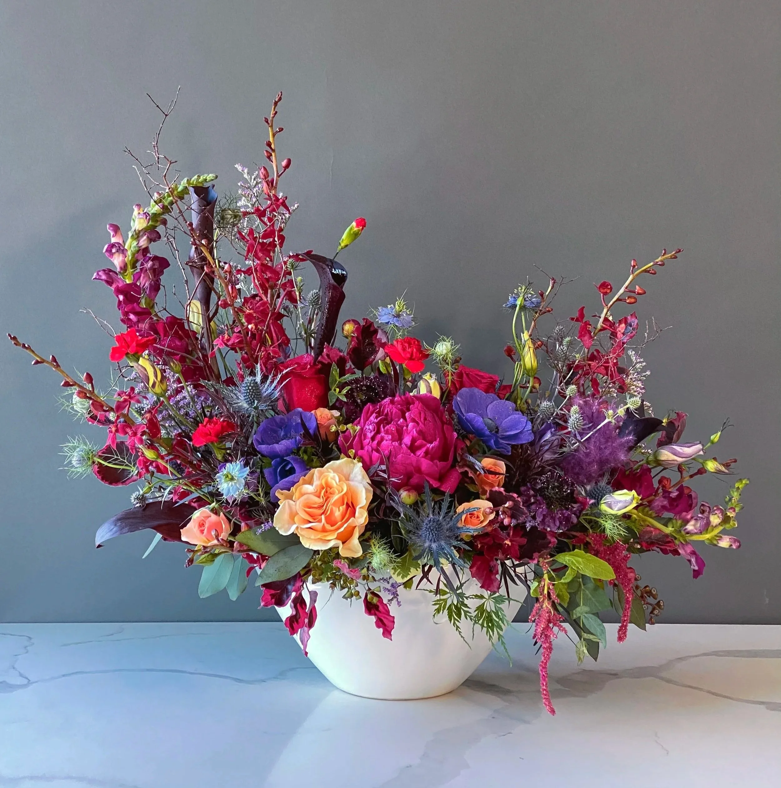 A colorful bouquet of assorted flowers in a white paper wrapping placed on a light-colored surface against a muted background.